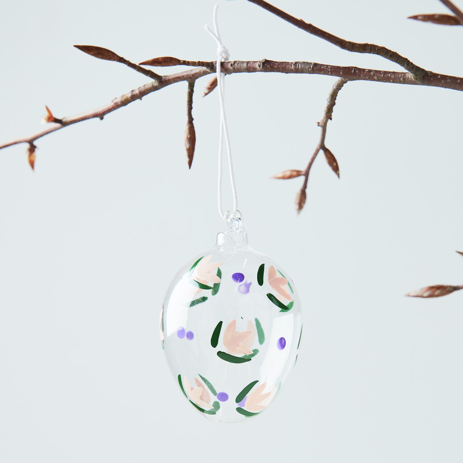 Glas Ei Blüten handbemalt, hängend an einem Ast, verziert mit floralen Mustern von Rico Design.