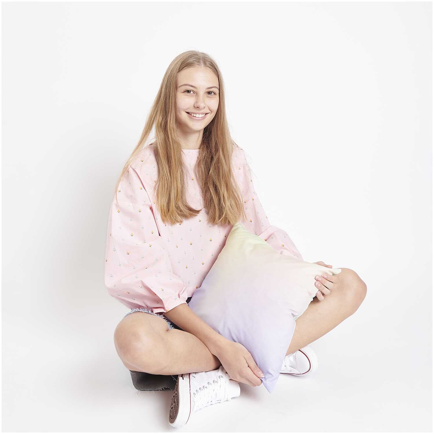 Stoffabschnitt Baumwoll-Popelin Pixel Blumen Rosa: Mädchen in rosa Oberteil mit Kissen, lächelnd auf weißem Hintergrund. Ideal für kreative Nähprojekte.
