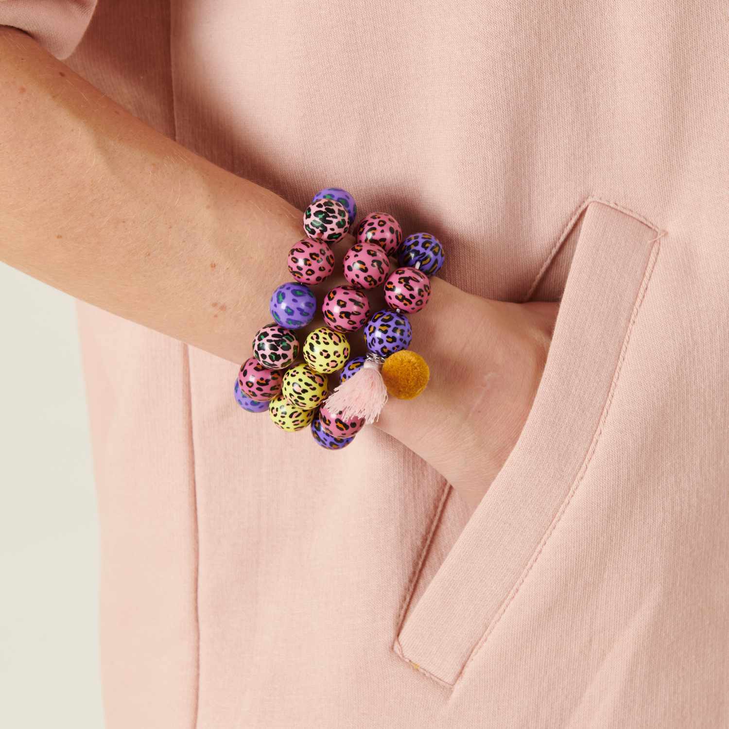 Bastelanleitung Acid Leo Armbänder: Bunte, leopardenmuster Armbänder am Handgelenk einer Person in rosa Kleidung.