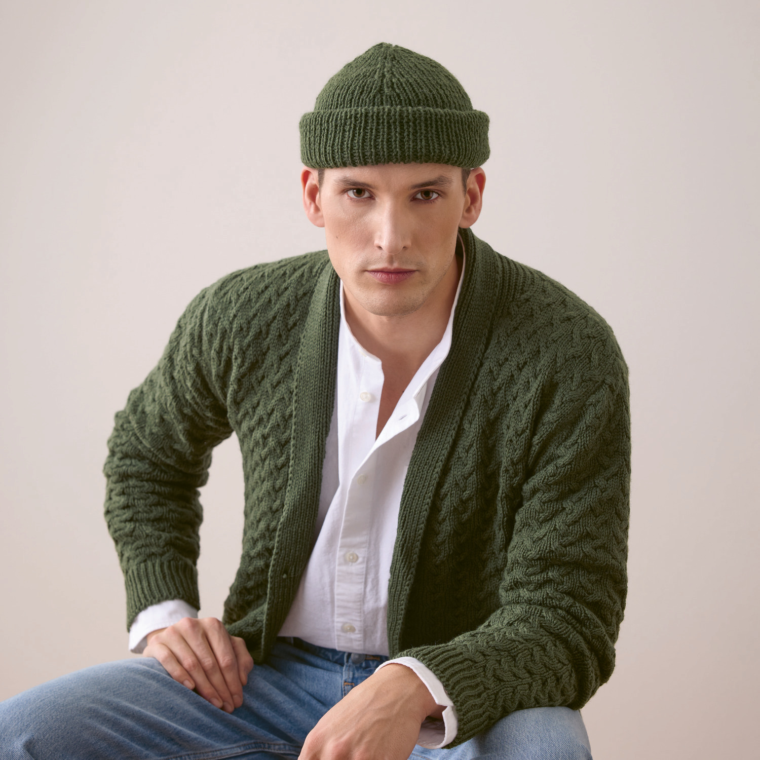 Strickset Herrenjacke Modell 27 aus Trachtenbuch I mog di: Grüner Strickjacke und Mütze, getragen von einem Mann in weißem Hemd und Jeans.