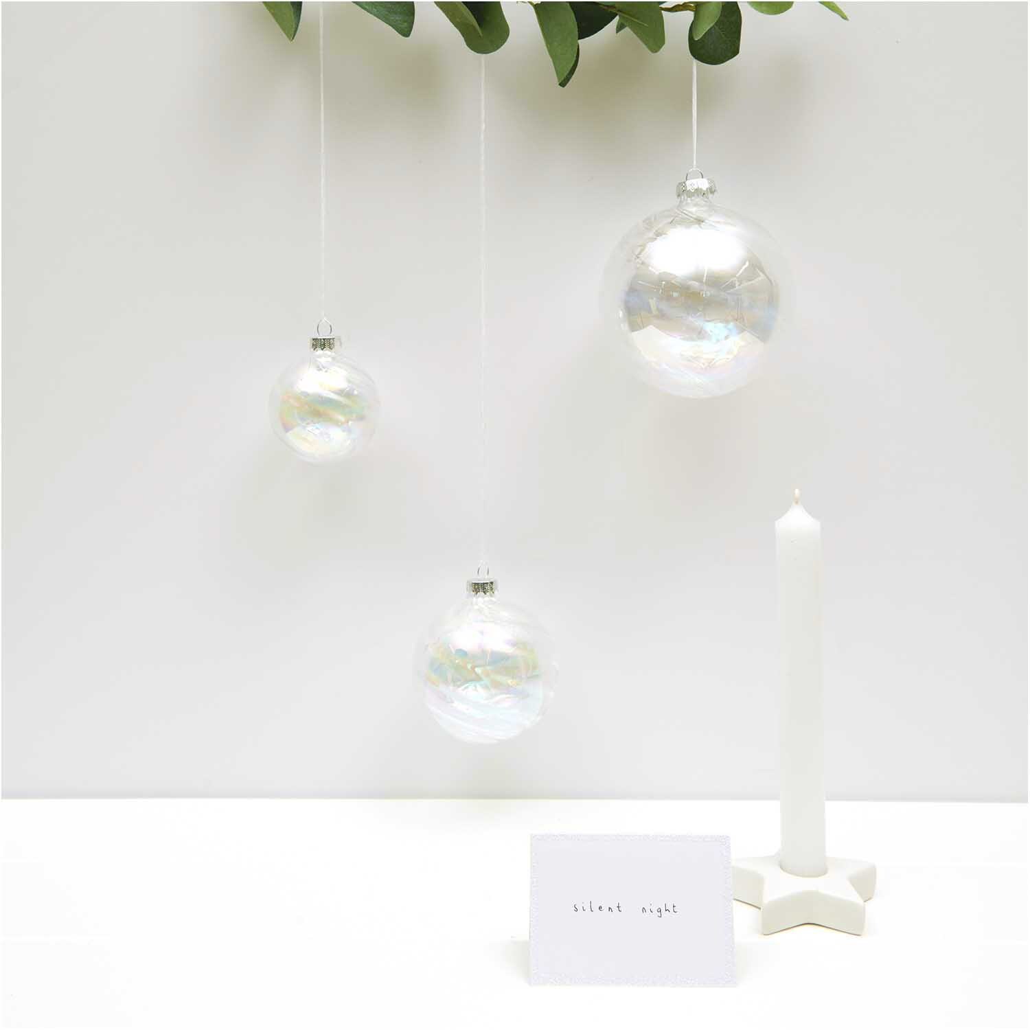 Baumschmuck Glaskugel klar-irisierend von Rico Design, hängend vor weißem Hintergrund mit Kerze.