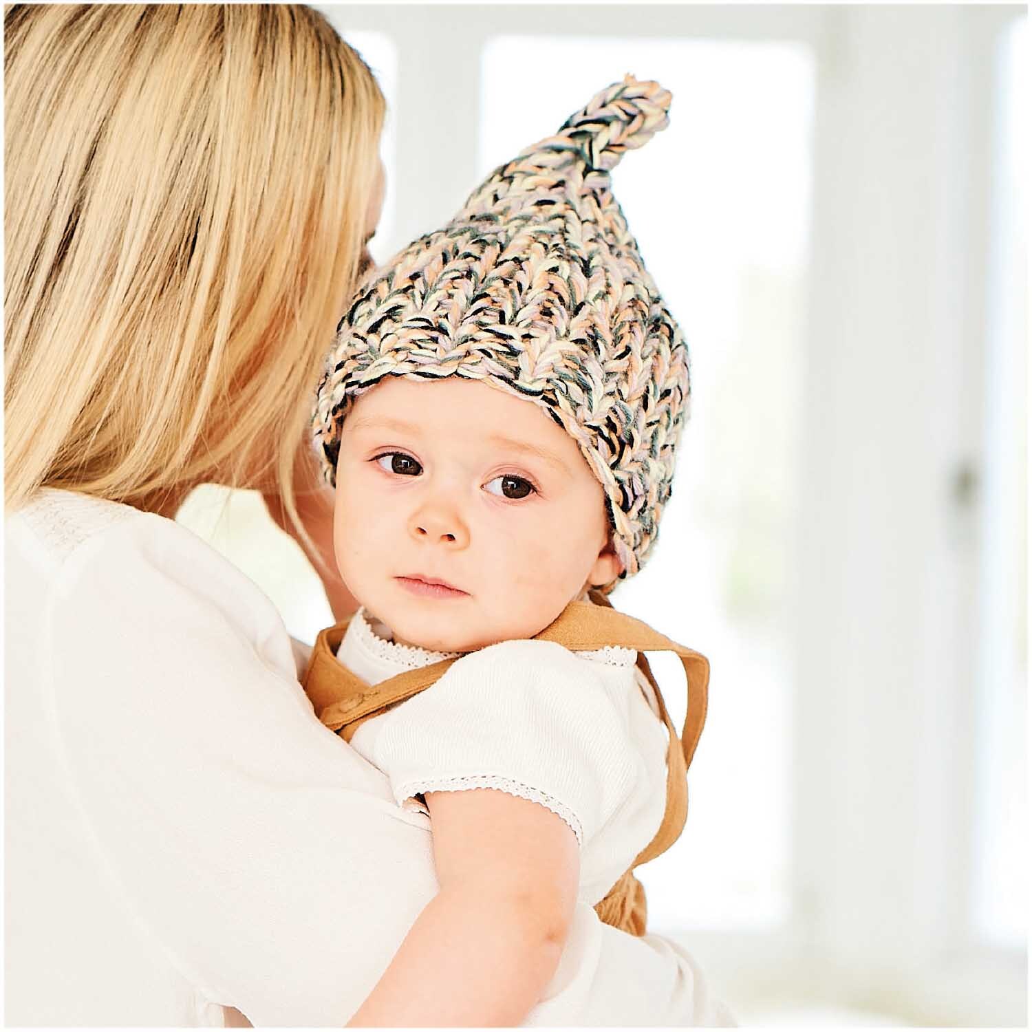 Rico Baby Dream dk uni - A Luxury Touch: Ein Baby mit gestrickter Mütze in sanften Farben, gehalten von einer Frau.