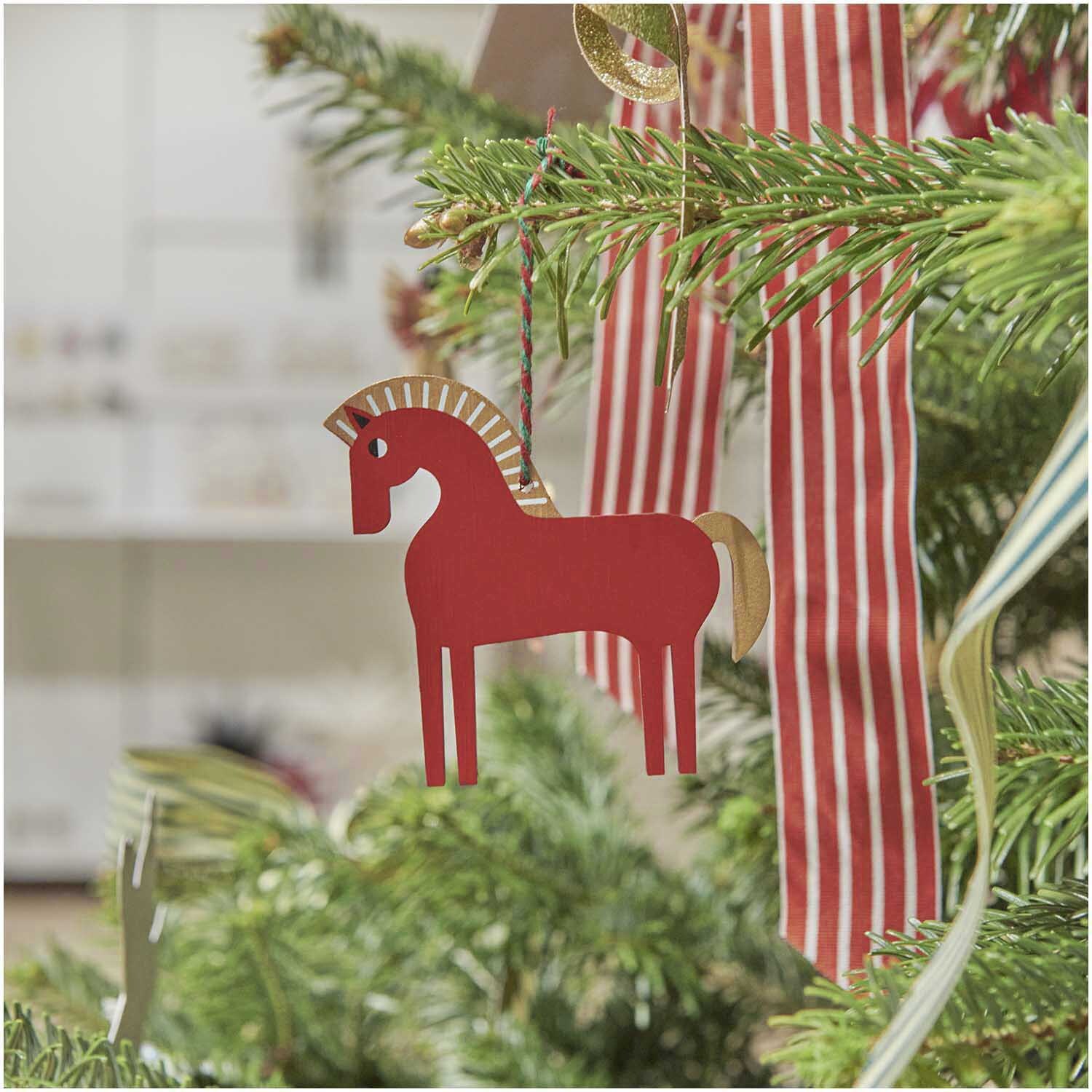 Hänger Holz-Pferd Rot von Rico Design schmückt einen Weihnachtsbaum. Größe: 9x4x8,4cm.