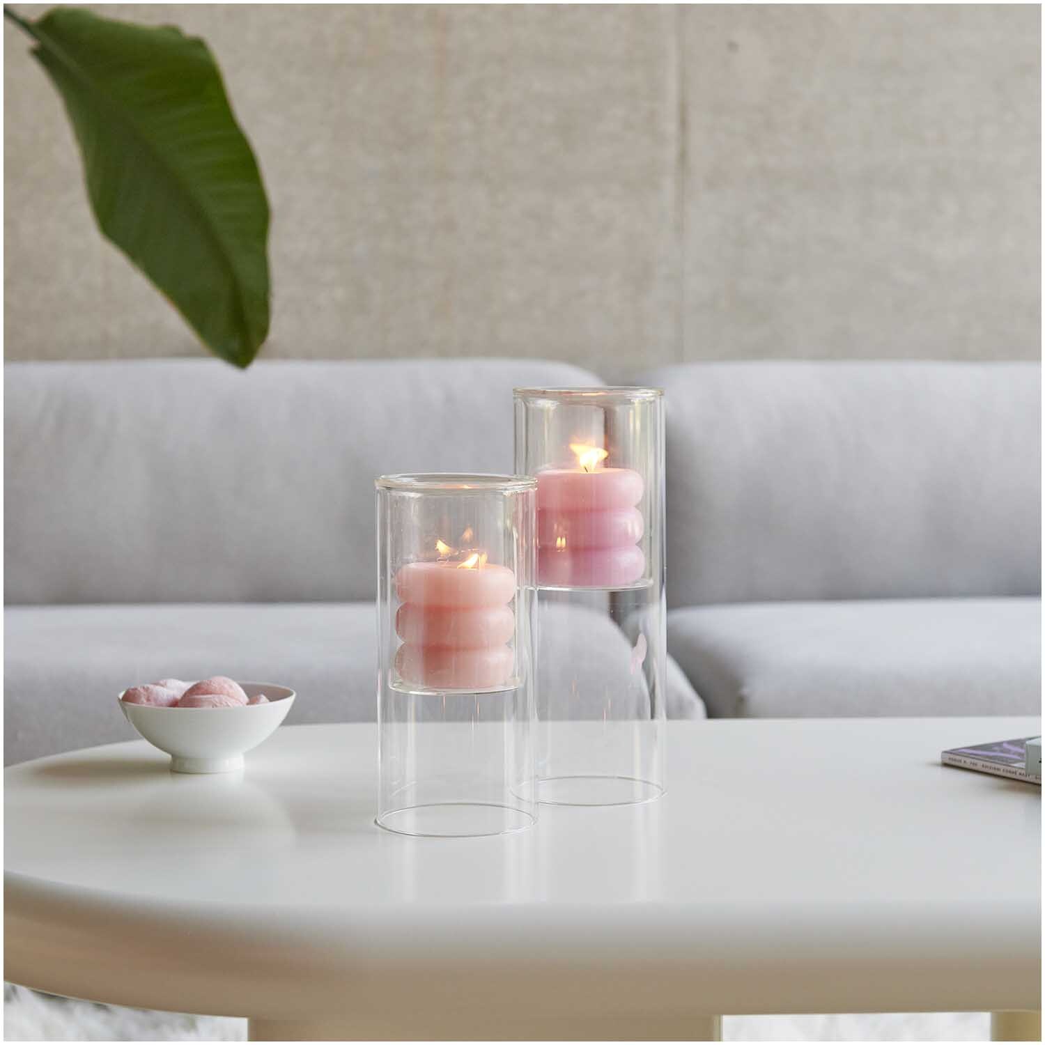 Glas-Windlicht mit brennenden Kerzen auf einem Tisch, umgeben von moderner Einrichtung.