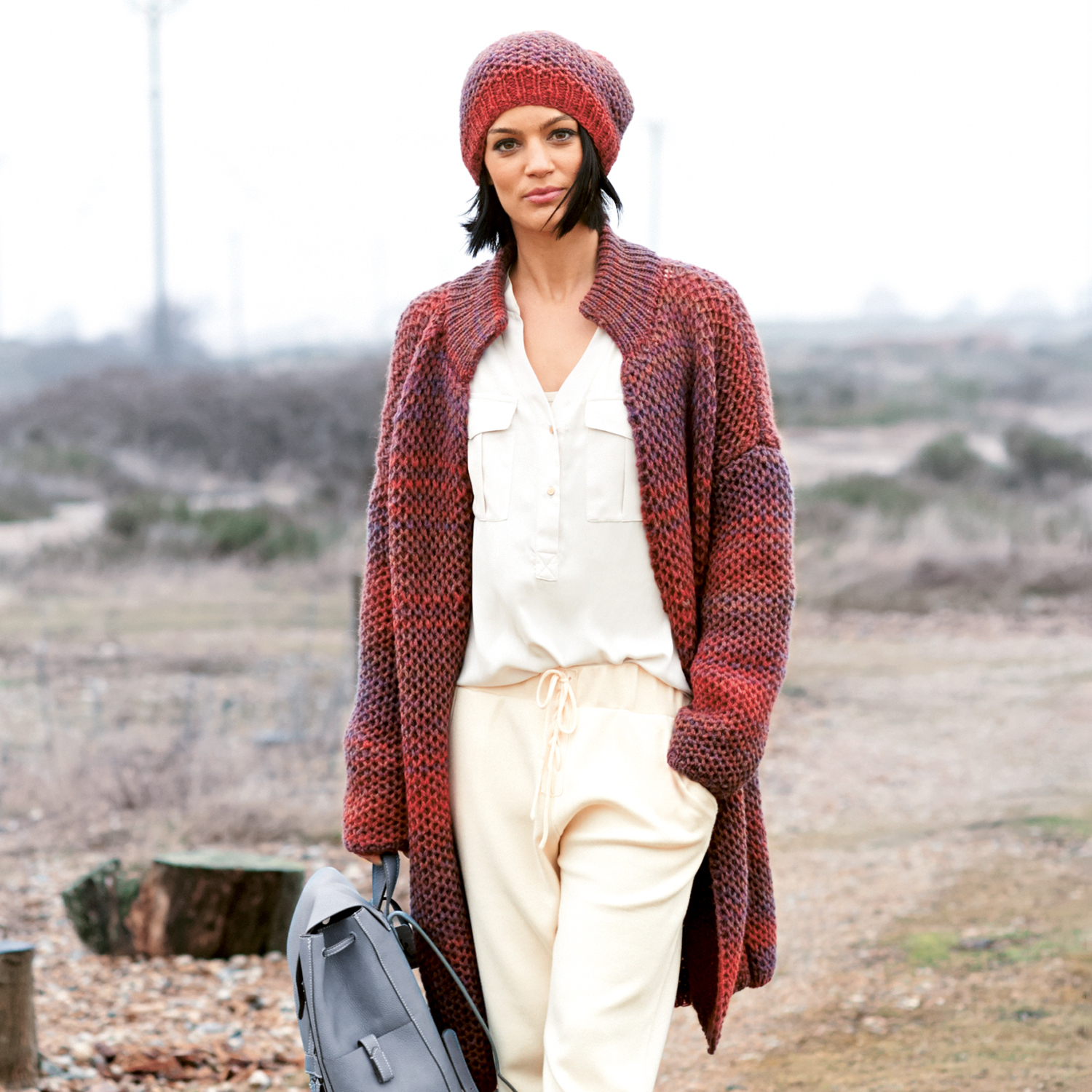 Strickanleitung Mütze und Jacke aus Creative Light Melange: Frau trägt rote Strickmütze und Jacke in ländlicher Umgebung.