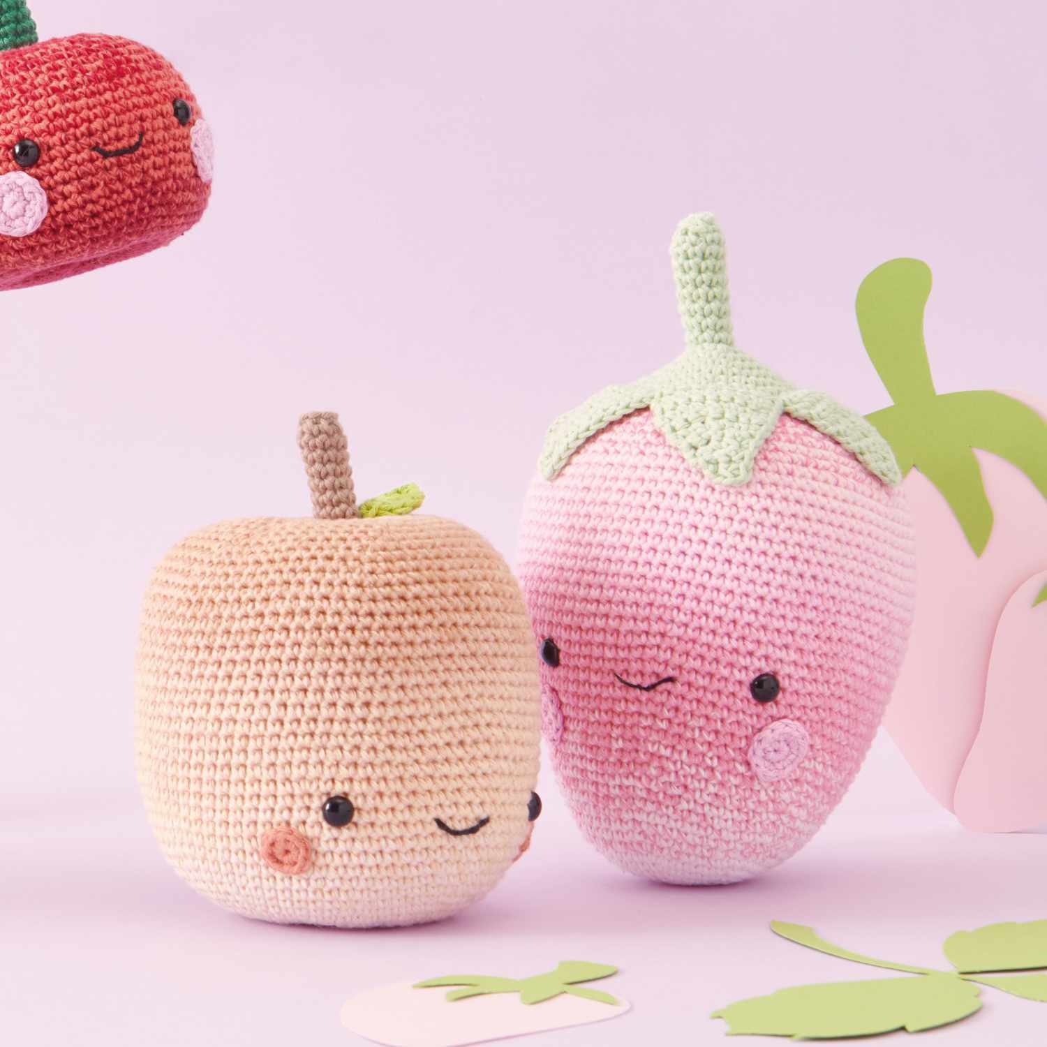 Häkelset Erdbeere aus Ricorumi Fresh Friends: Niedliche gehäkelte Erdbeere und Apfel auf rosa Hintergrund. Ideal für kreative Bastelprojekte.