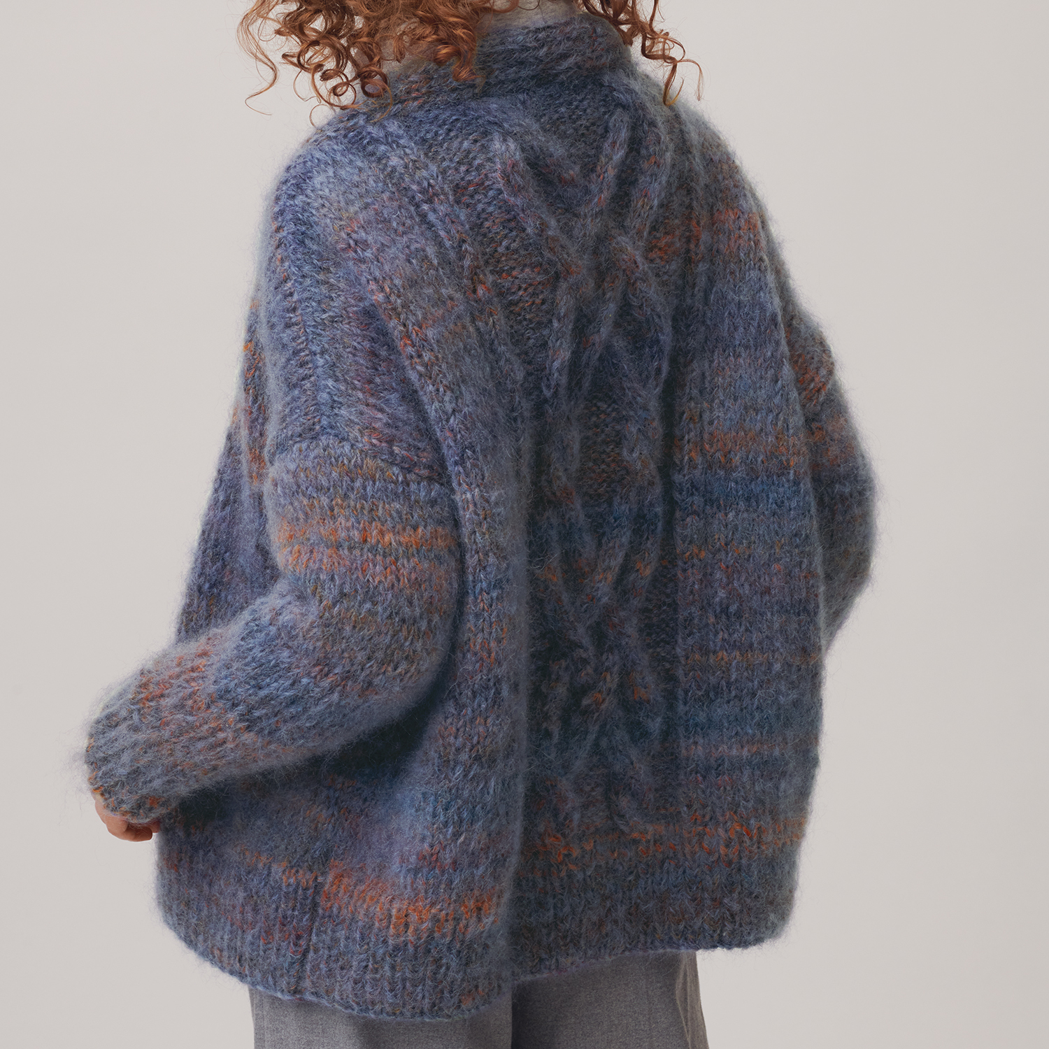 Strickanleitung Zopf-Jacke aus Creative Mohair Melange: Frau trägt eine blaue, melierte Strickjacke mit Zopfmuster.