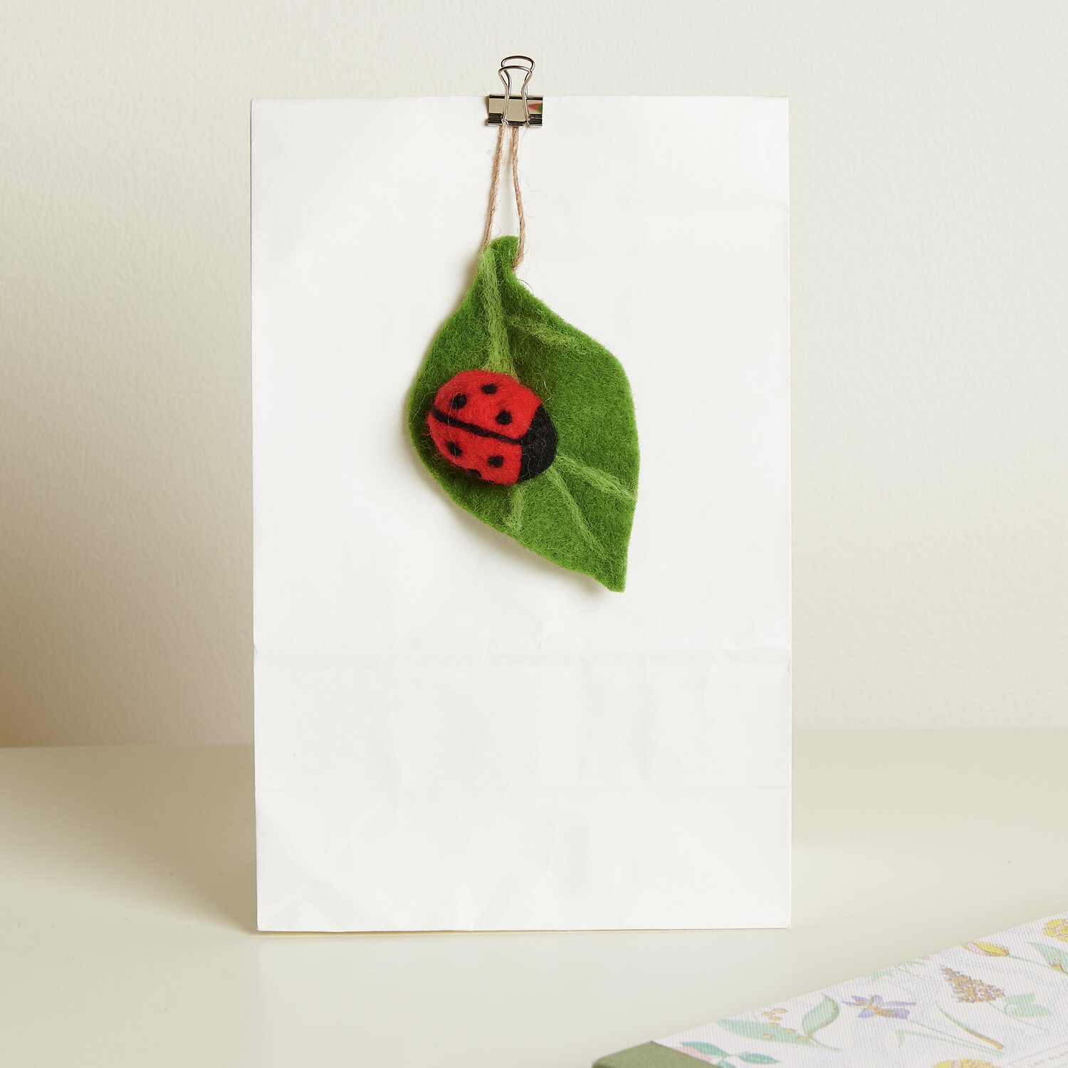 Aufhänger Filz-Blatt mit Marienkäfer: Grünes Filzblatt mit rotem Marienkäfer, dekorativ an weißer Wand befestigt. Größe: 10x6,5x2,4cm.