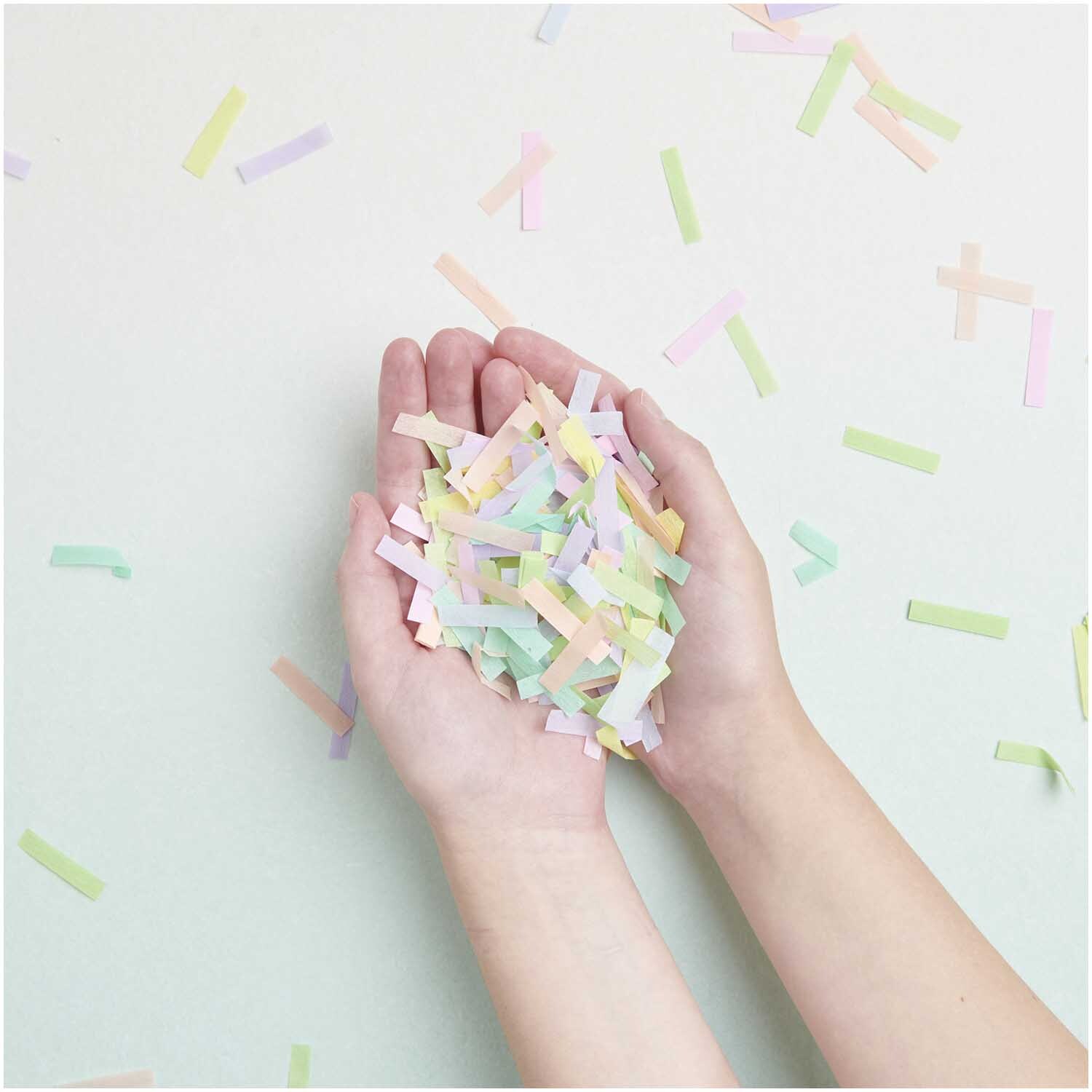 Krepp-Konfetti Regenbogen Pastell Mix in Händen gehalten, ideal für kreative Dekorationen.