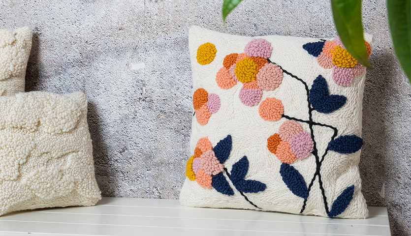 Anleitung florales Punch Needle Kissen mit bunten Blumenmotiven auf weißem Hintergrund.