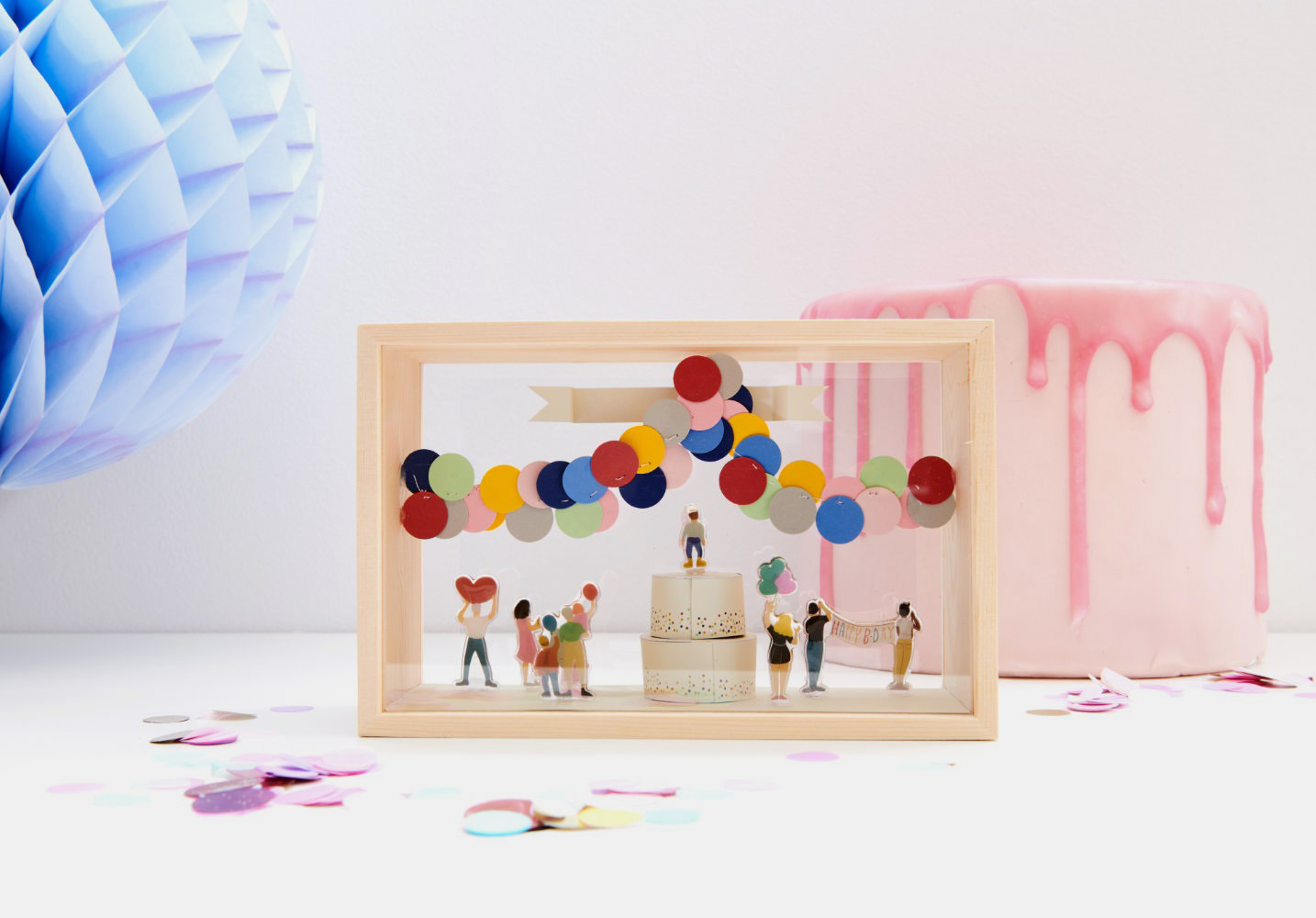 Objektkasten mit gebastelter Torte, bunter Luftballon-Girlande und verschiedenen Mini-Figuren.