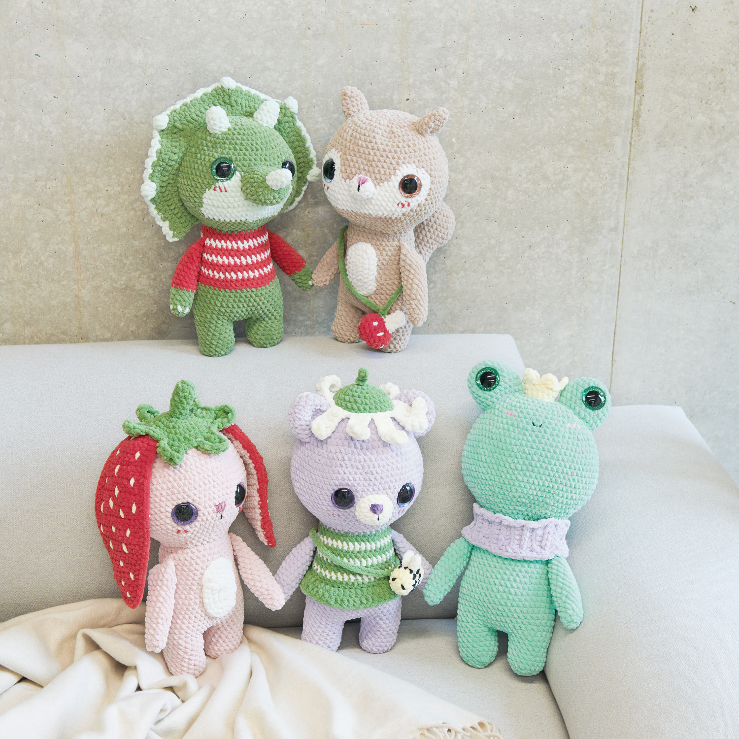 Häkelset Baby Dinosaur Modell 01: Fünf bunte, gehäkelte Tiere aus Chenillove Big Cuties auf einem Sofa.