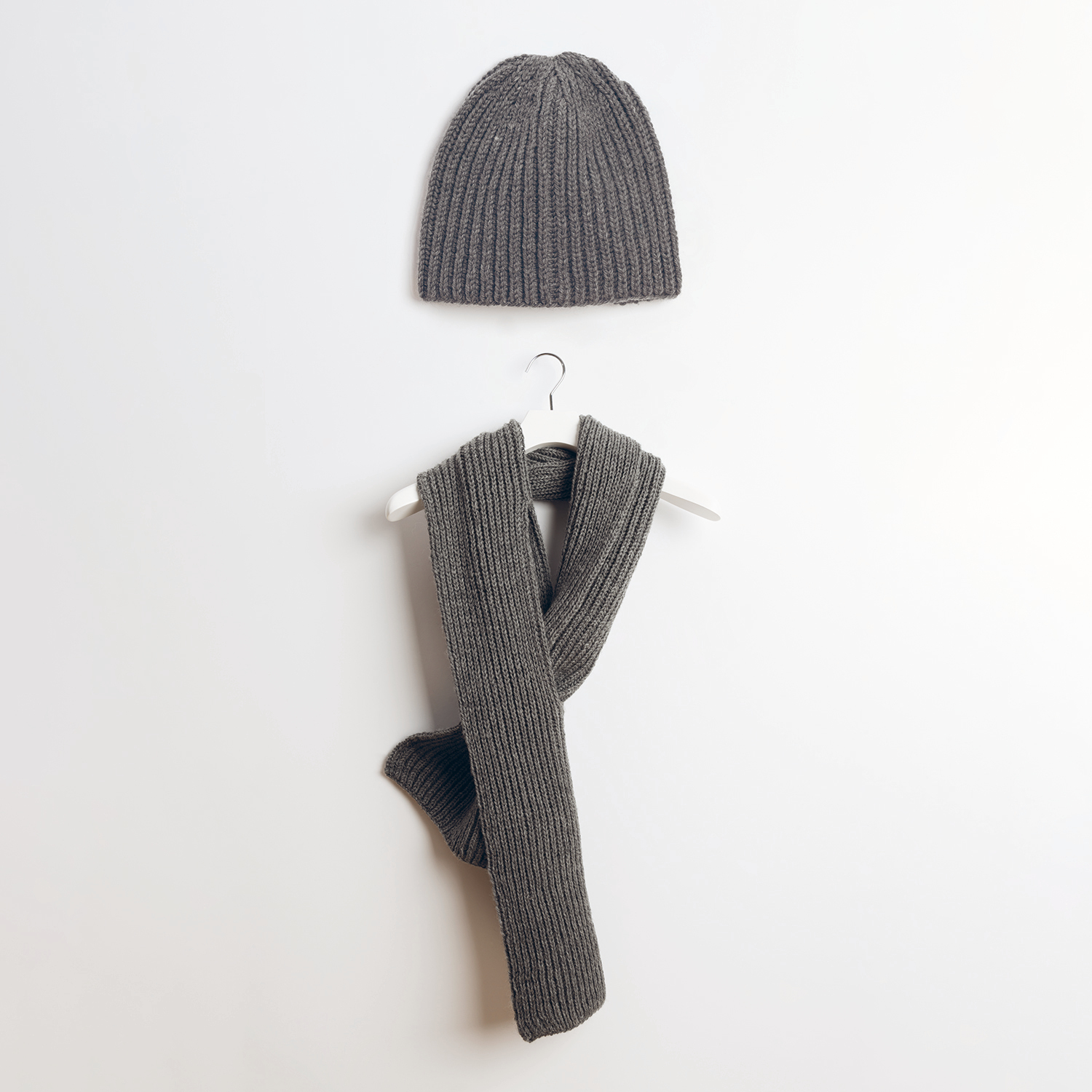 Strickanleitung Mütze und Schal aus Essentials Soft Merino aran: Graue, gerippte Mütze und Schal auf weißem Hintergrund, elegant drapiert.