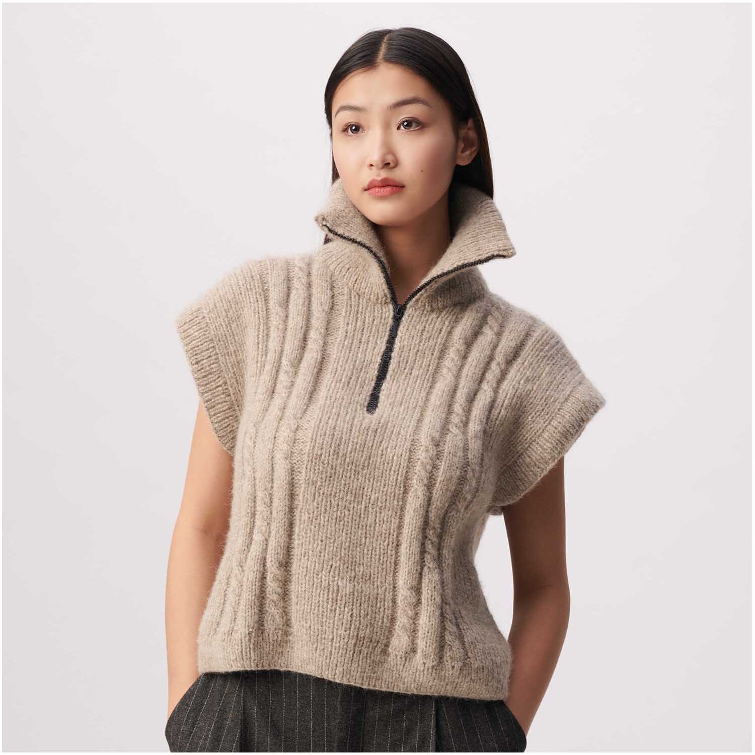 Strickset Pullunder Modell 26 aus Luxury Knits Winter Special: Beiger Pullunder mit Reißverschluss und Stehkragen, getragen von Frau vor grauem Hintergrund.