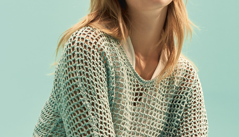 Häkelanleitung Pullover aus Mille Fili Glitz: Frau trägt luftigen, mintfarbenen Netzpullover vor türkisfarbenem Hintergrund.