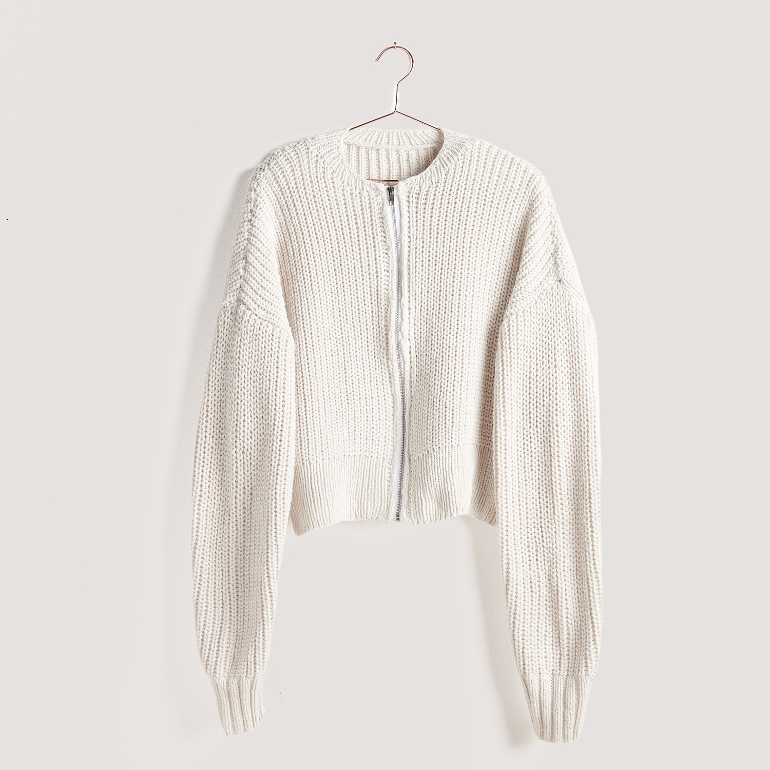 Strickset Jacke Modell 14 aus Vegan Cashmere: Weiße Strickjacke mit Reißverschluss, hängend an einem Kleiderbügel. Ideal für stilvolle, nachhaltige Mode.