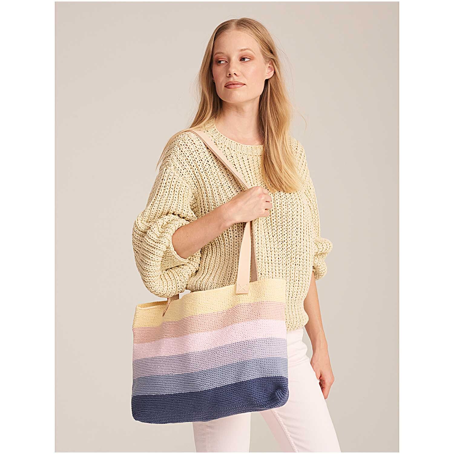 Creative Cotton aran: Frau mit gestricktem Pullover und gestreifter Tasche in Pastelltönen, ideal für Freizeit.