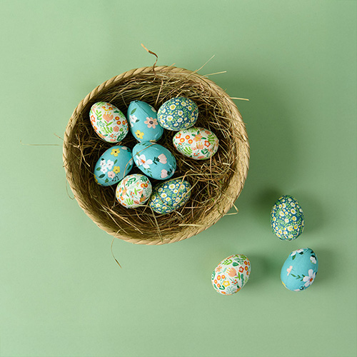Ostereier mit blau, grünem Blumenmuster in braunem Osternest mit Gras. Flatlay von Produkten.