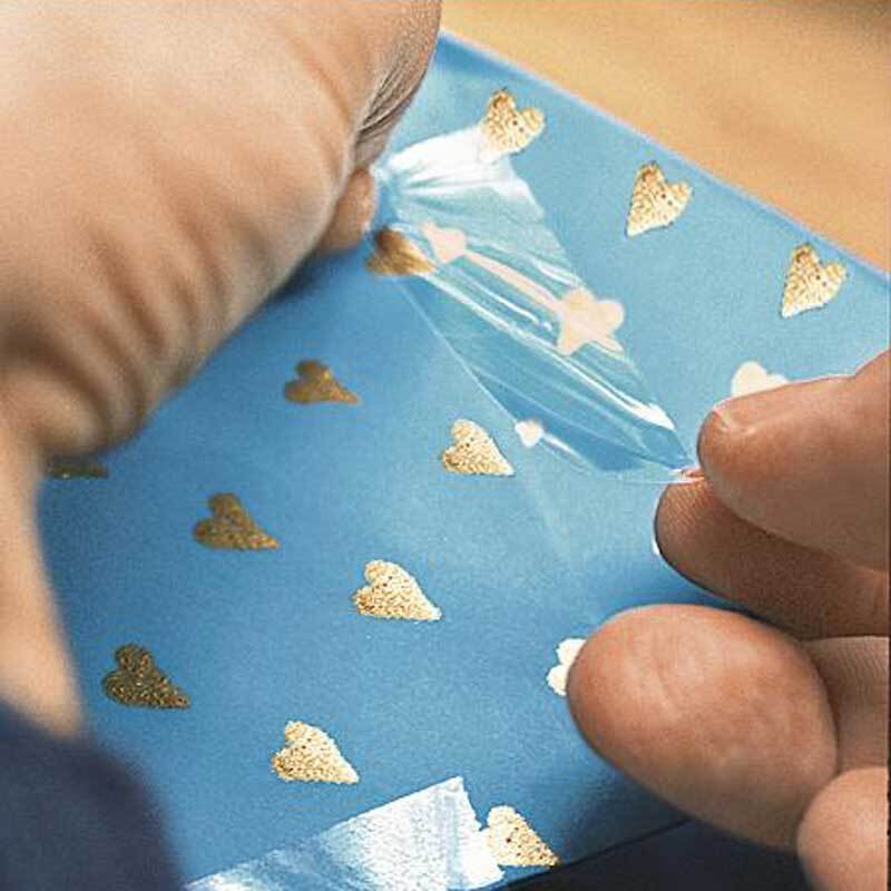 tesa film® klar Klebefilm wird auf blauem Papier mit goldenen Herzen aufgetragen. Ideal für präzises und unsichtbares Kleben.
