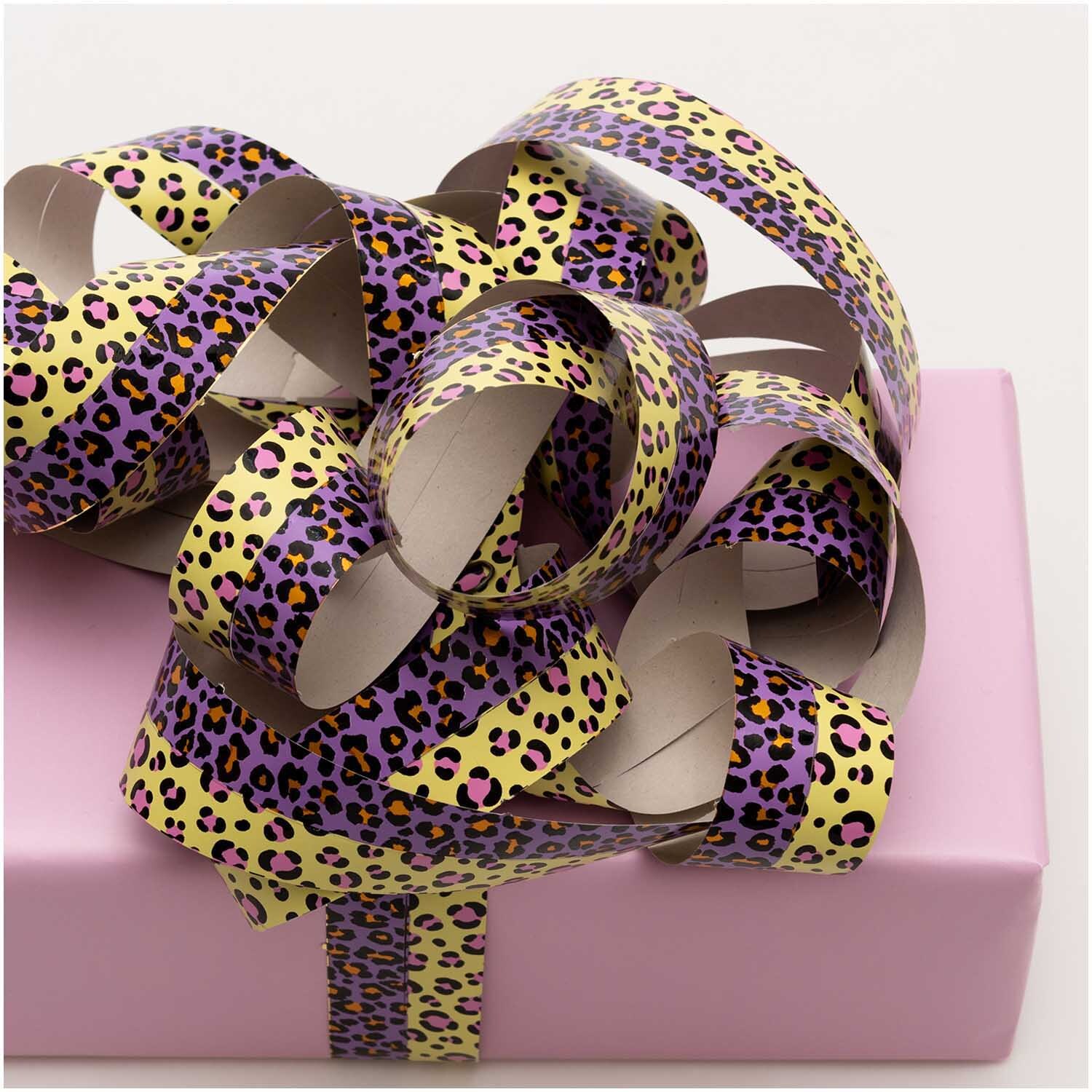 Luftschlangen Acid Leo gold 3,8m von Rico Design auf einem rosa Geschenk, mit Leopardenmuster in Lila und Gelb.