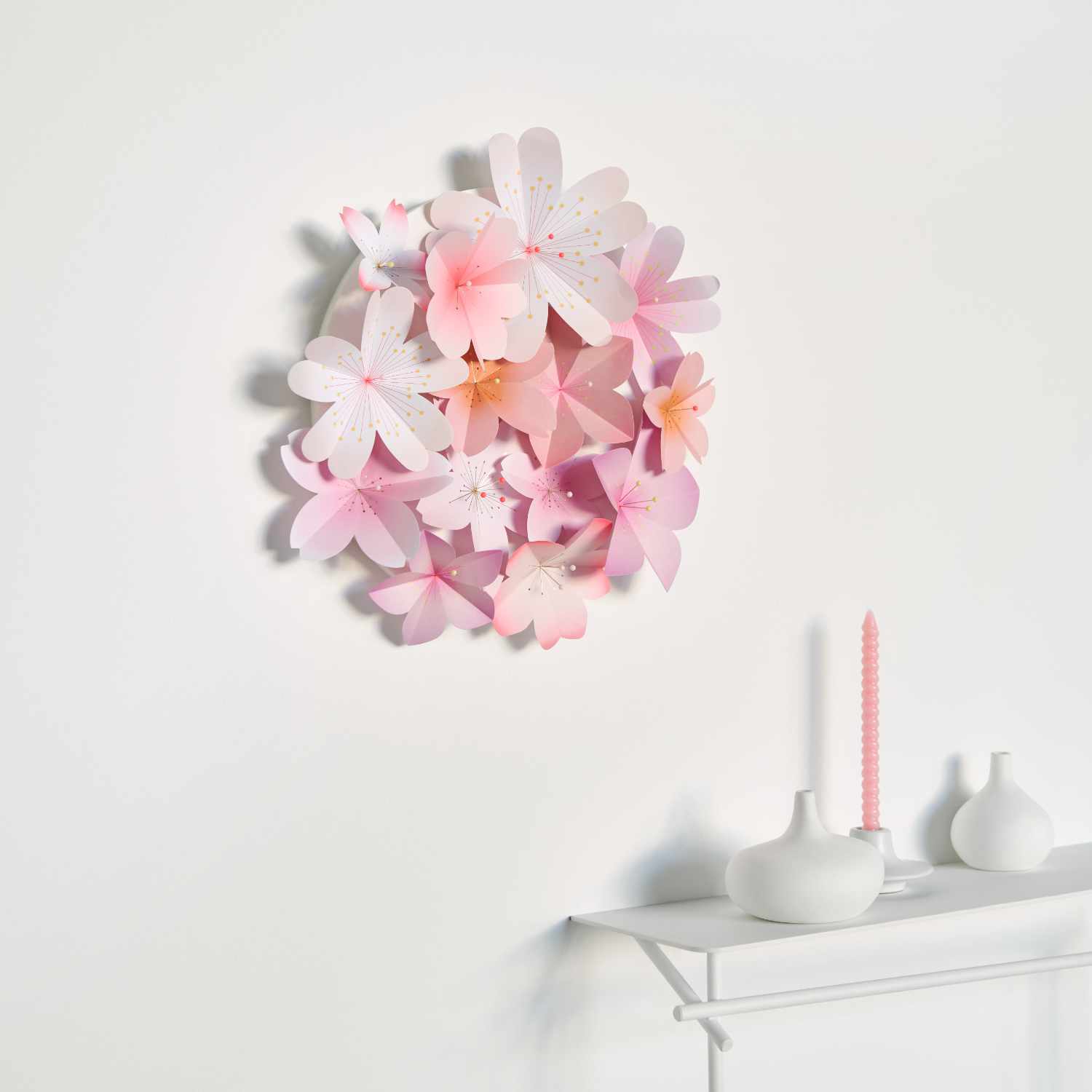 Bastelanleitung 3D-Papierblütenbild: Ein rundes Arrangement aus rosa und weißen Papierblüten an einer weißen Wand.