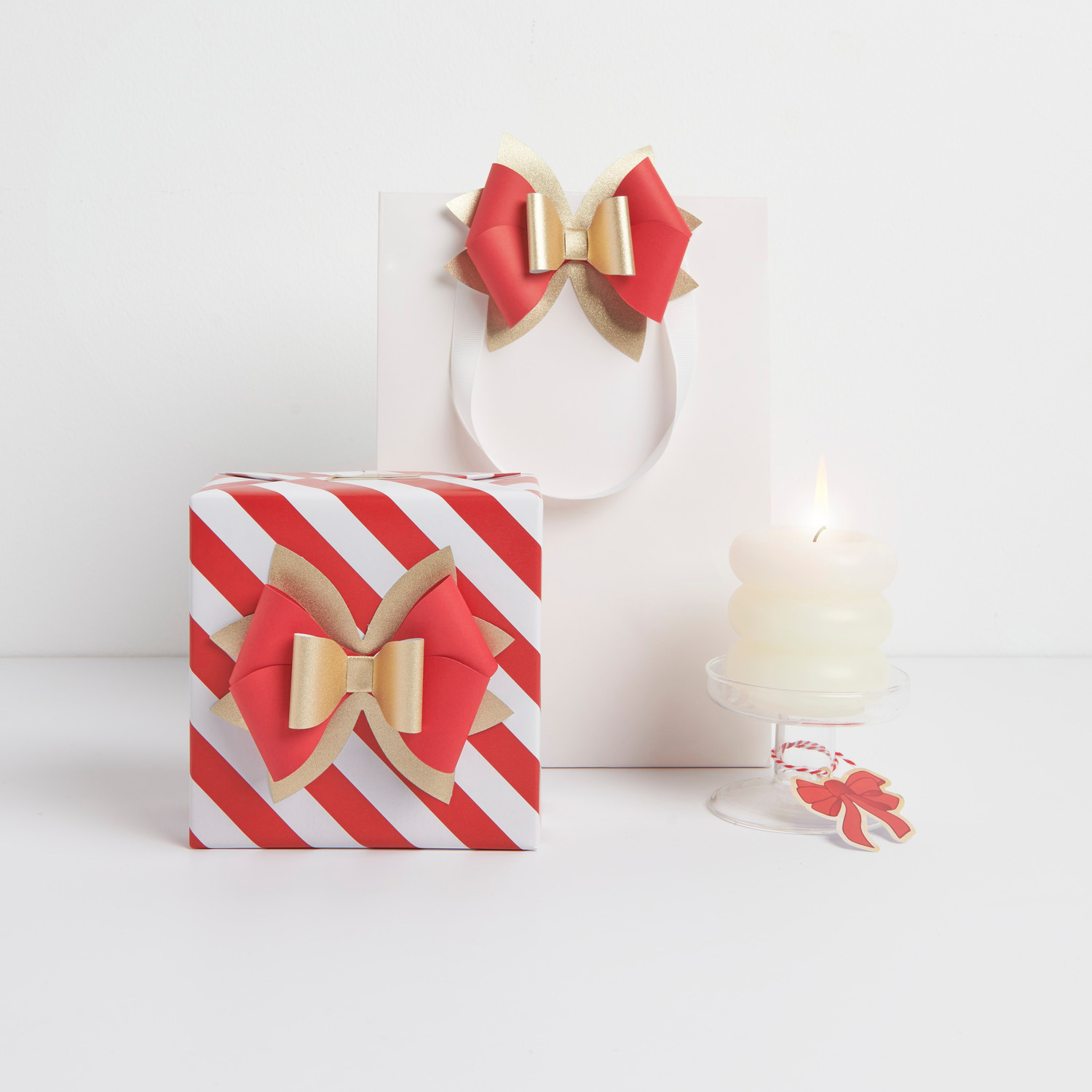Papierschleife Rot/Gold von Rico Design auf Geschenk und Tüte, dekoriert mit Kerze.