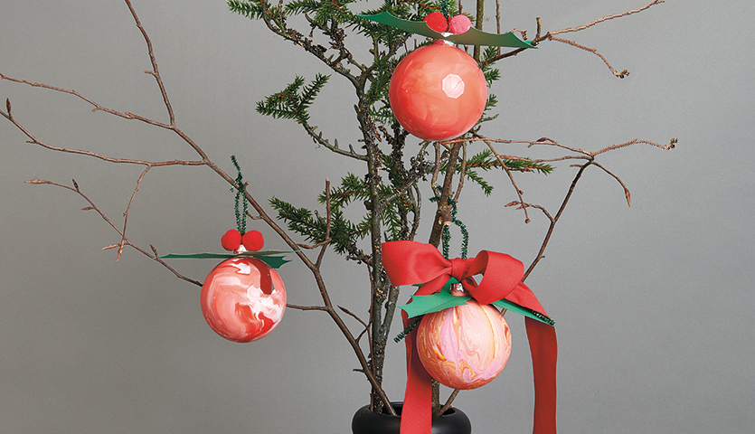 Anleitung Christbaumkugeln mit Pouring gestalten: Drei rote Kugeln an einem kahlen Zweig, verziert mit Schleifen und Blättern.