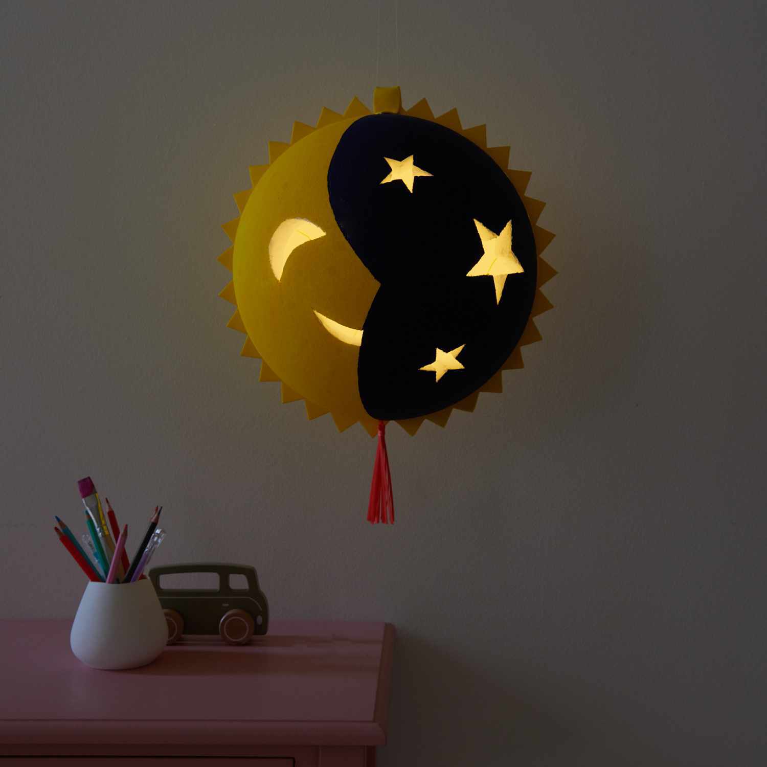 Bastelanleitung Sonne Mond Laterne: Eine leuchtende Laterne mit Sonne, Mond und Sternen an der Wand.