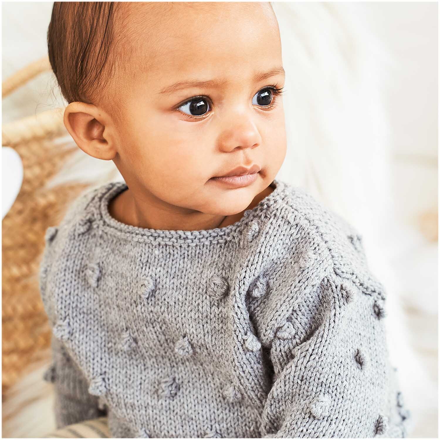 Rico Baby Classic dk: Ein Baby trägt einen gestrickten Pullover in Silber Melange, weich und gemütlich.