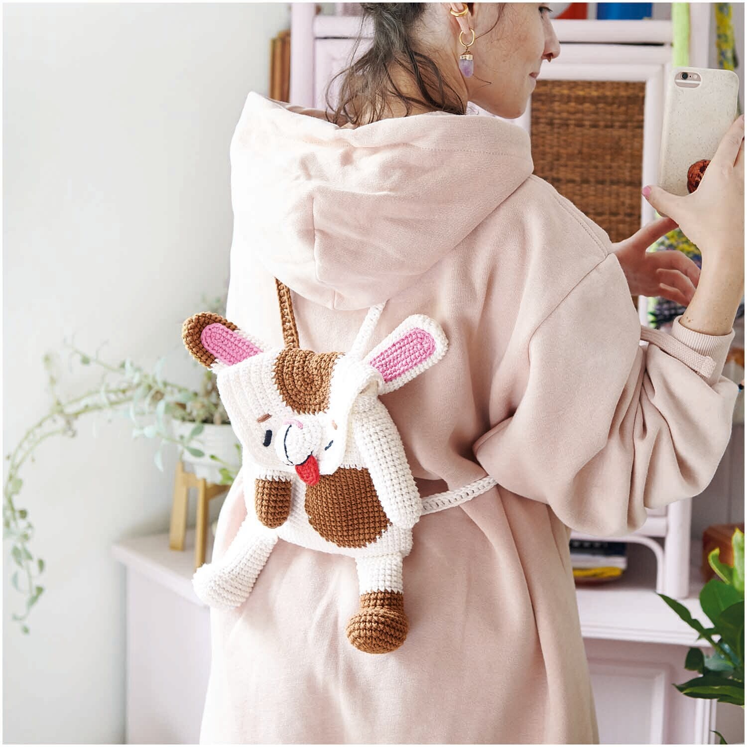 Creative Cotton aran: Frau mit rosa Kapuzenpullover trägt gehäkelten Hasen-Rucksack aus weißem Garn.