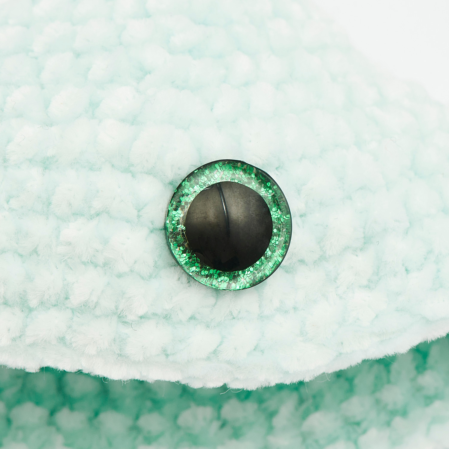 Sicherheitsaugen-Set für Kuscheltiere, 12mm, zeigt ein grünes Auge auf weichem, hellgrünem Stoff. Ideal für DIY-Projekte.