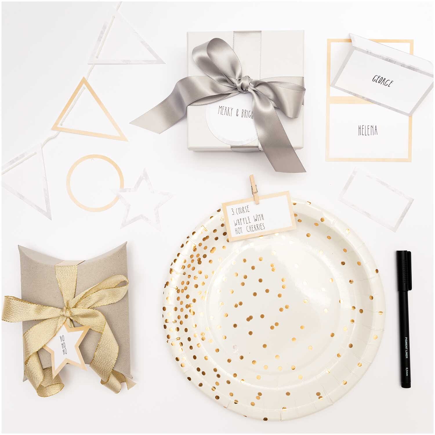 Paper Poetry Papierwimpel mit Hot Foil, dekoriert mit goldenen und silbernen Akzenten, umgeben von Geschenken und Schreibutensilien.