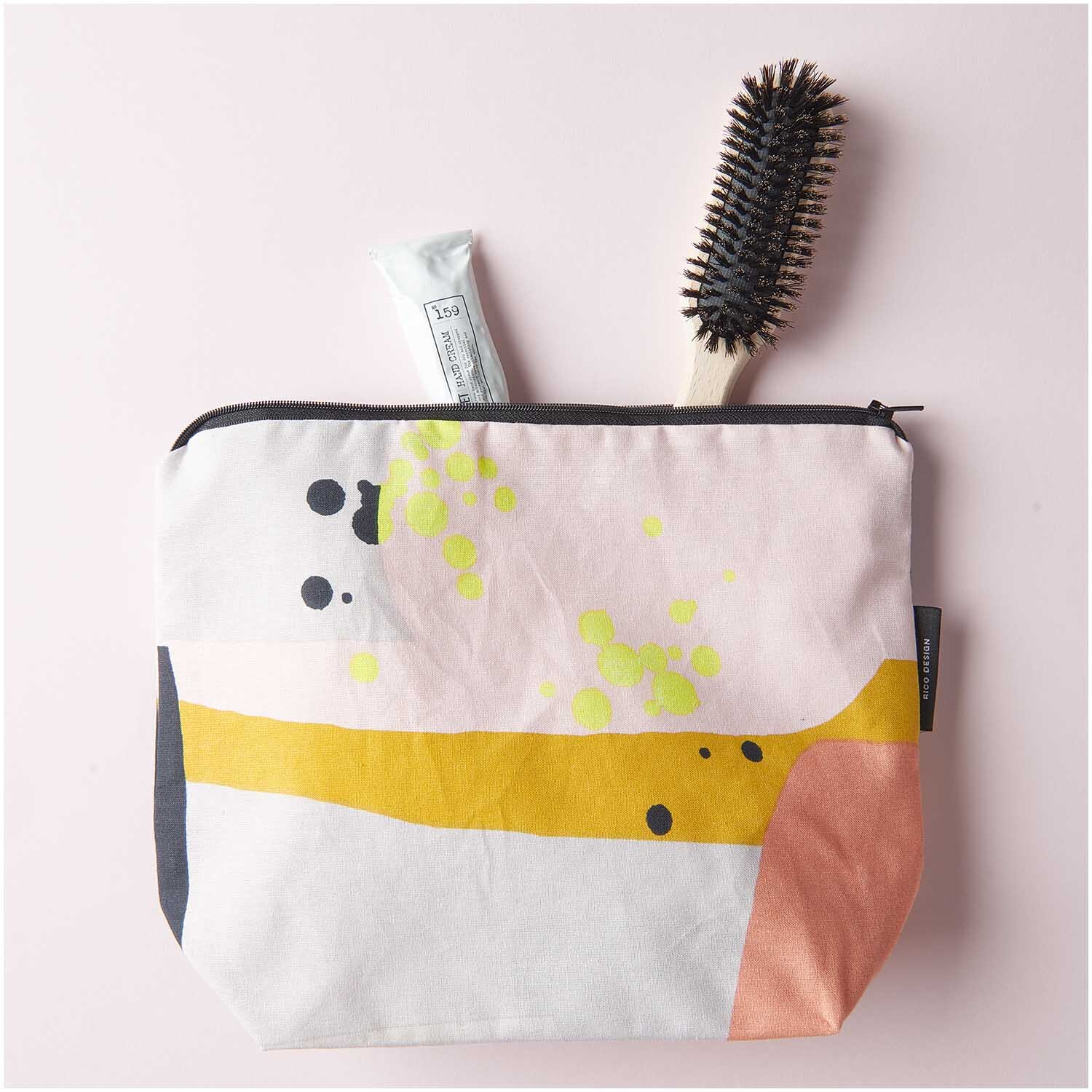 Kosmetiktasche Okina Hana mit grafischem Print, gefüllt mit Bürste und Tube, auf rosa Hintergrund.