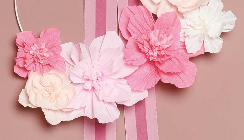 Bastelanleitung Blumenkranz aus Krepppapierblumen: Ein Kranz aus rosa und weißen Krepppapierblumen auf rosa Hintergrund.