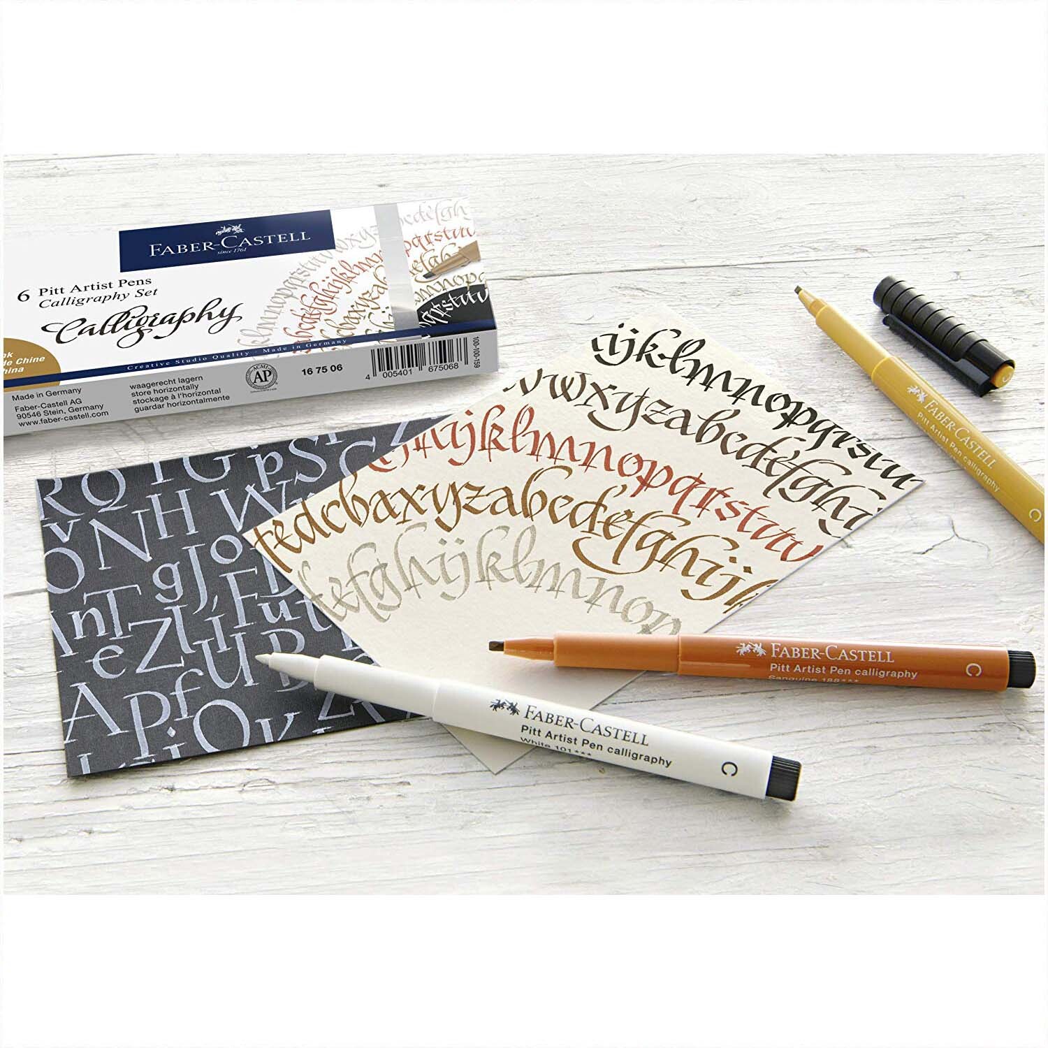 Tuschestift Pitt Artist Pen Calligraphy 6 Stück von Faber Castell, mehrfarbig, auf einem Tisch mit kalligrafischen Schriftproben.