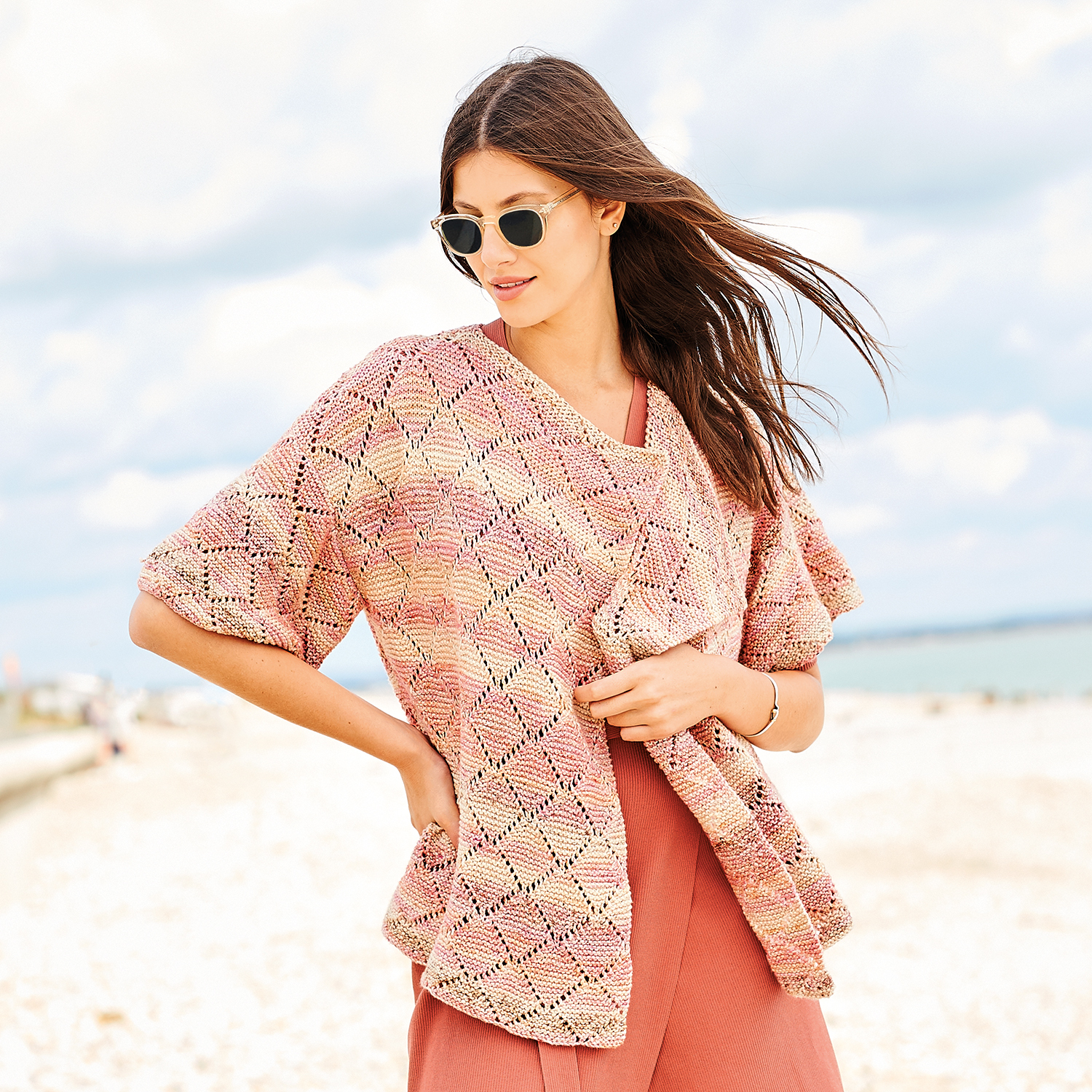 Strickanleitung Jacke aus Fashion Cotton Double Printed dk: Frau am Strand mit rosa gemusterter Strickjacke und Sonnenbrille.