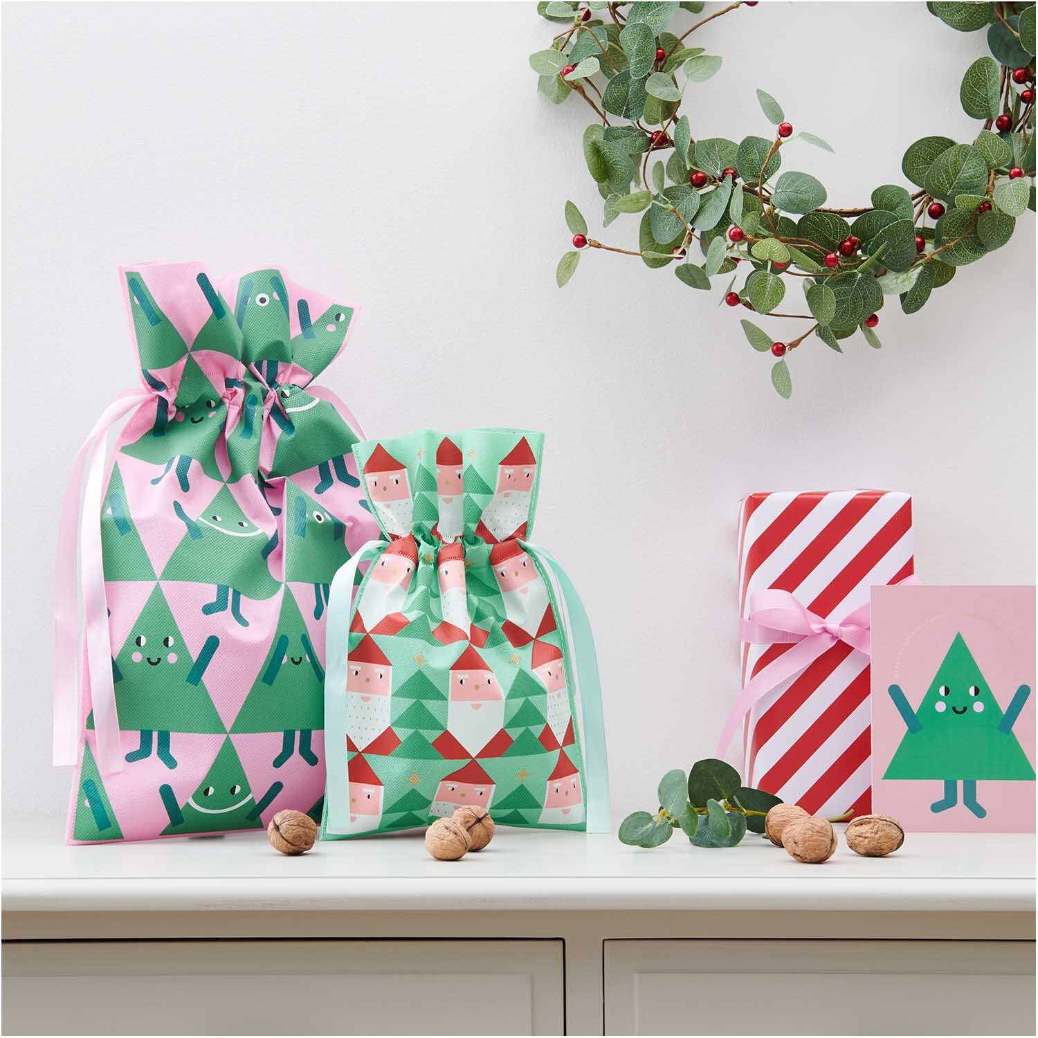 Geschenktüte Tannen groß 30x45cm: Bunte Geschenktüten mit Tannenbaum-Motiven, umgeben von Nüssen und Dekoration.