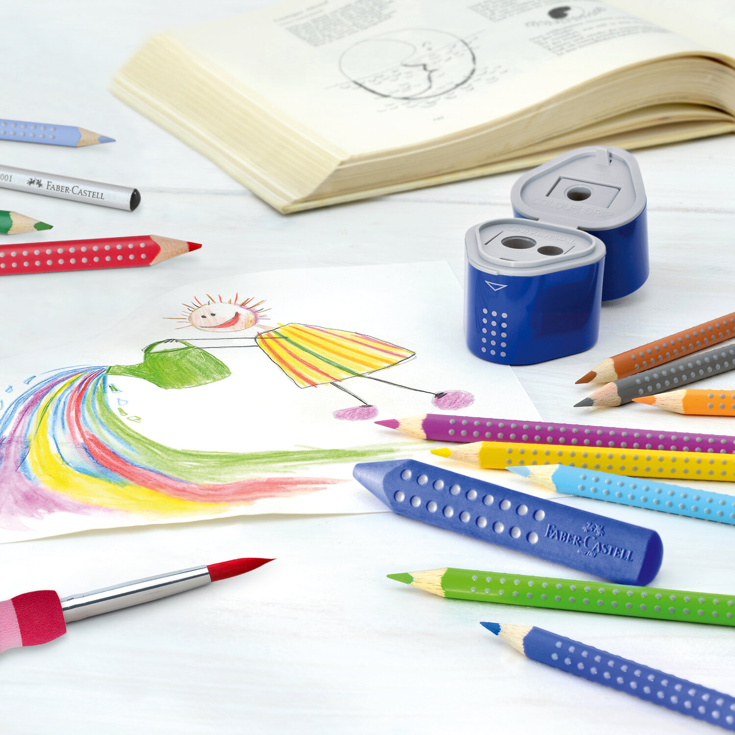 Colour Grip 2001: Bunte Faber Castell Stifte und Anspitzer auf einem Tisch mit Kinderzeichnung.