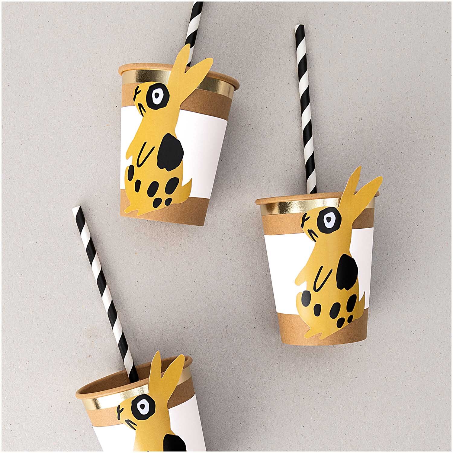 Papiermanschetten Hase weiß 6 Stück: Drei Becher mit Hasenmotiv und schwarz-weißen Strohhalmen.