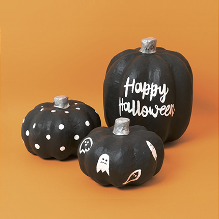 Drei unterschiedliche Pappmaché Kürbisse schwarz angemalt und mit weißen Halloween Motiven gestaltet. Fotosetting oranger Hintergrund.