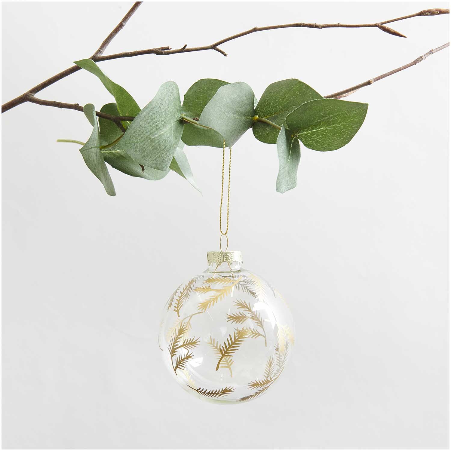 Glaskugel Baumschmuck mit Tannenzweigen, hängend an einem Ast, verziert mit goldenen Details.