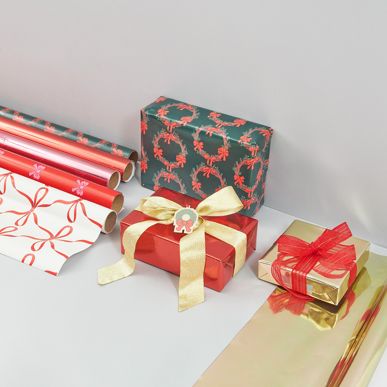 Weihnachtlich verpackte Geschenke und verschiedene Geschenkpapierrollen. Fotosetting graue Ecke.