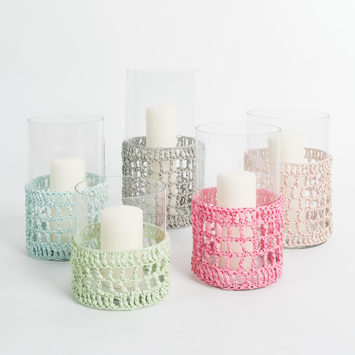 Häkelanleitung Windlichter Doppelstäbchen aus Creative Paper: Sechs Windlichter mit gehäkelten Hüllen in Pastellfarben umgeben weiße Kerzen in Glasgefäßen.