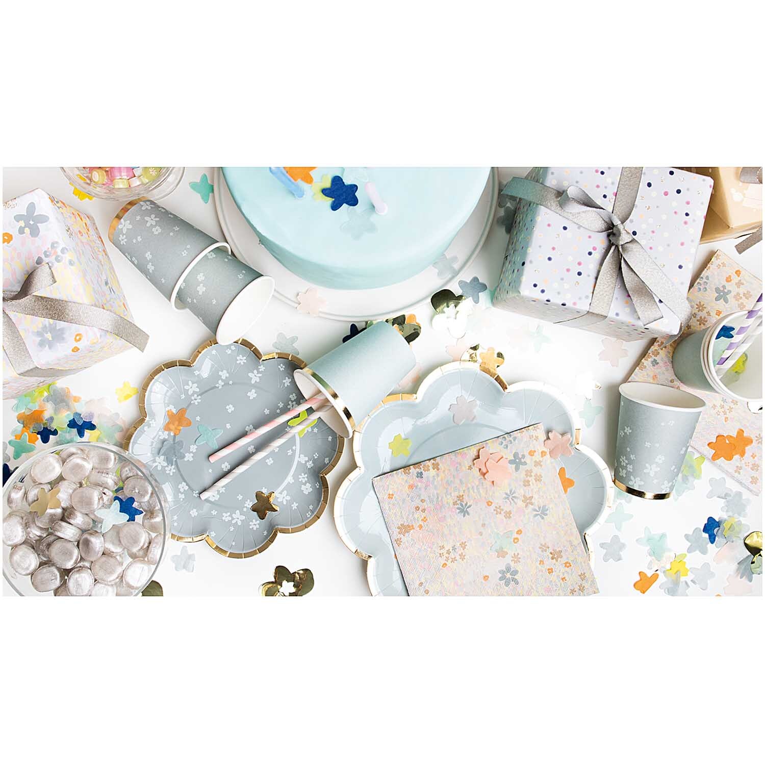 Konfetti Blüten blau Mix 20g: Festliche Tischdekoration mit blauen Blütenkonfetti von Rico Design, umgeben von Partygeschirr und Geschenken.