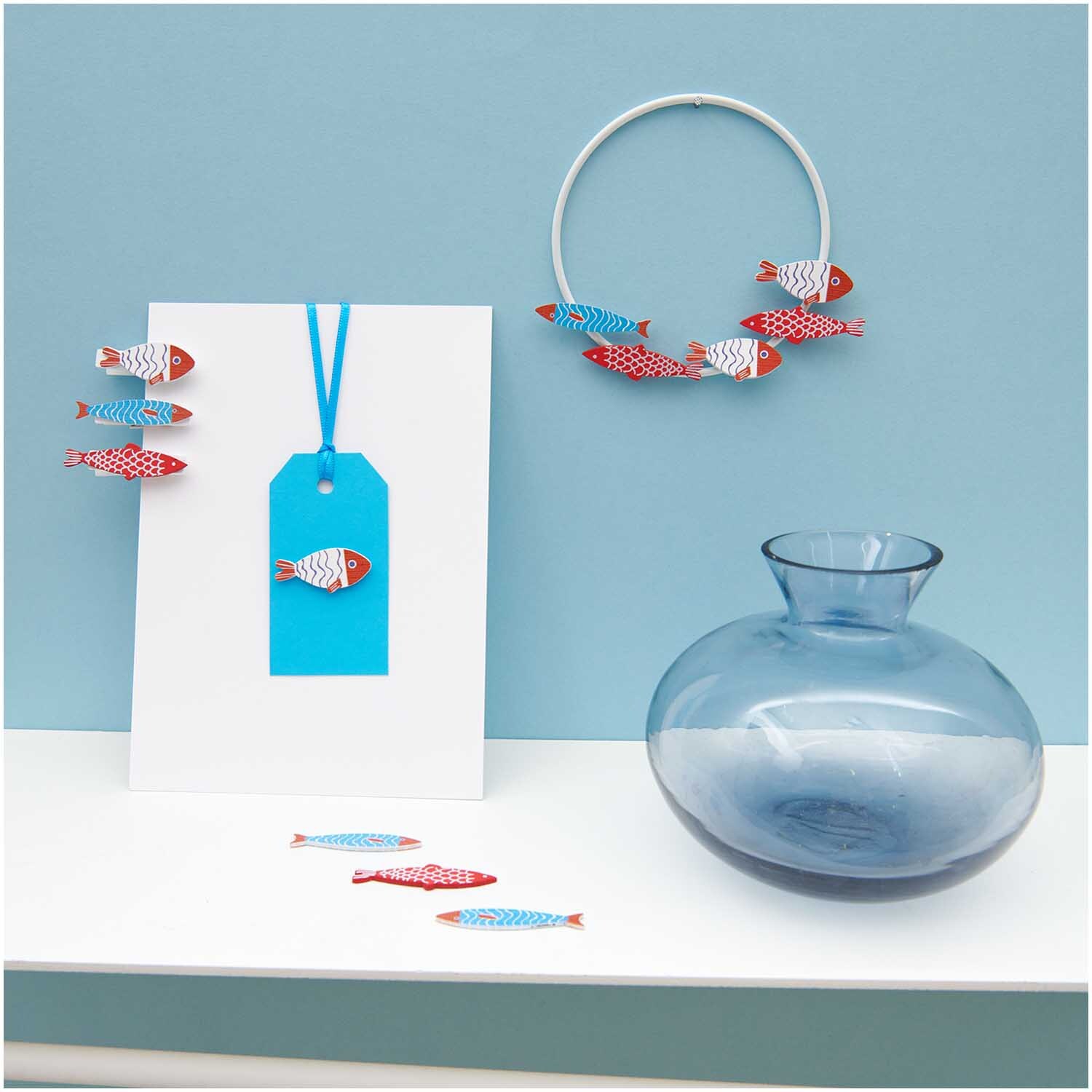 Dekoklammern Fisch Mix in rot-blau, dekorativ an einer Karte und einem Ring arrangiert, von Rico Design.
