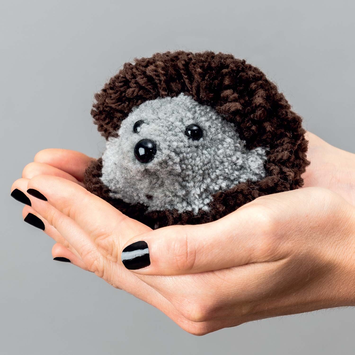 Bastelanleitung Pompon-Igel: Ein grauer und brauner Pompon-Igel liegt in Händen, ideal für DIY-Projekte.