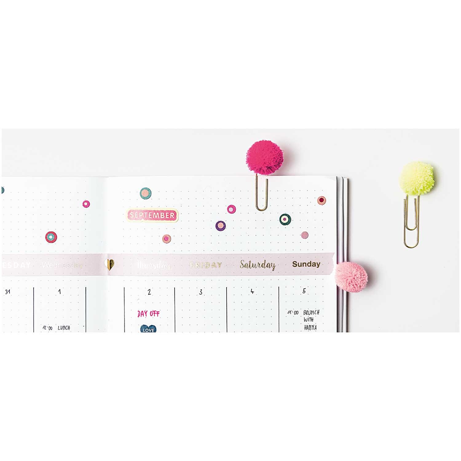 Paper Poetry Büroklammern mit Pompons in Pink und anderen Farben verzieren einen Kalender.