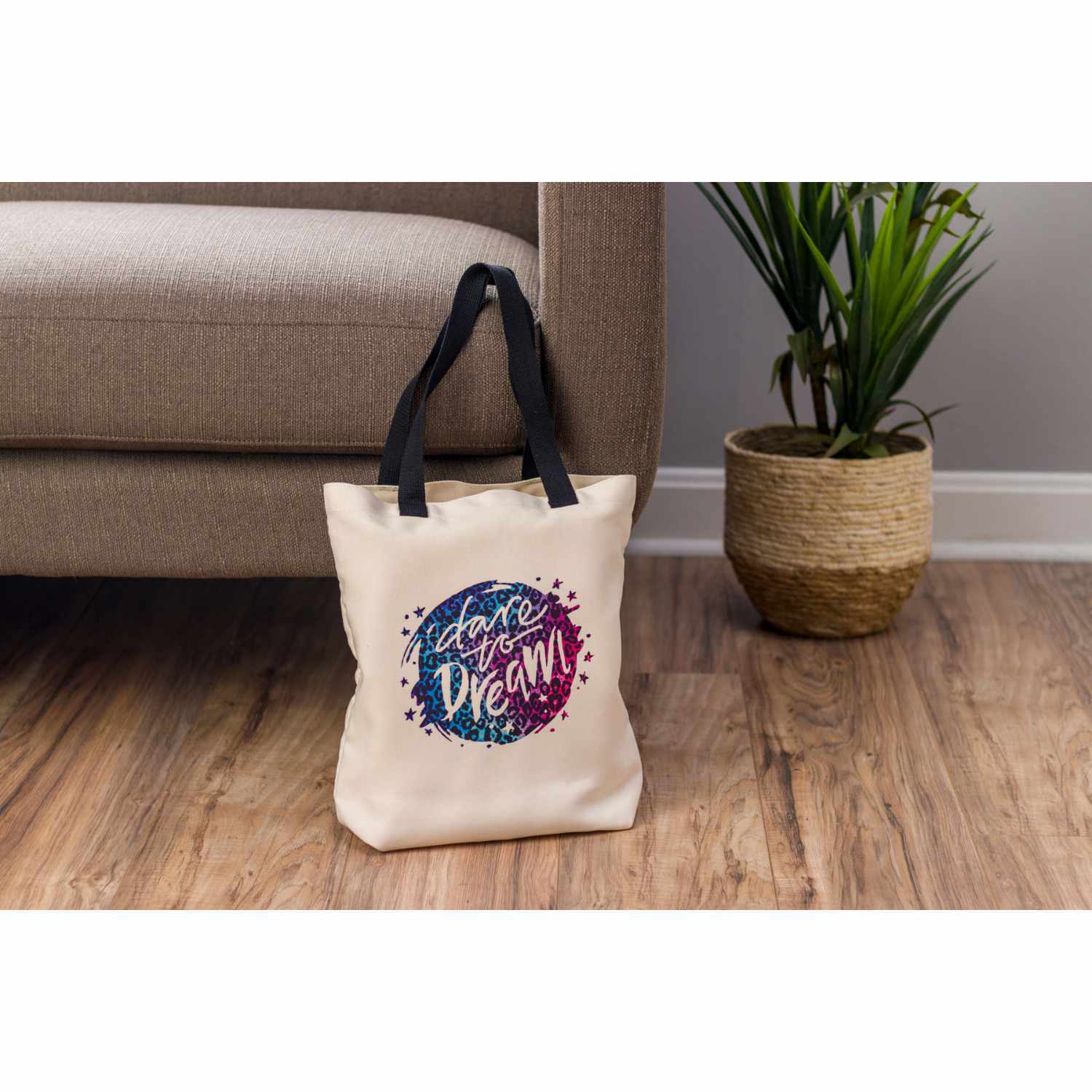 Einkaufstasche natur 48x35,5cm mit schwarzem Griff und buntem "Start Your Dream"-Design, neben einem Sofa.
