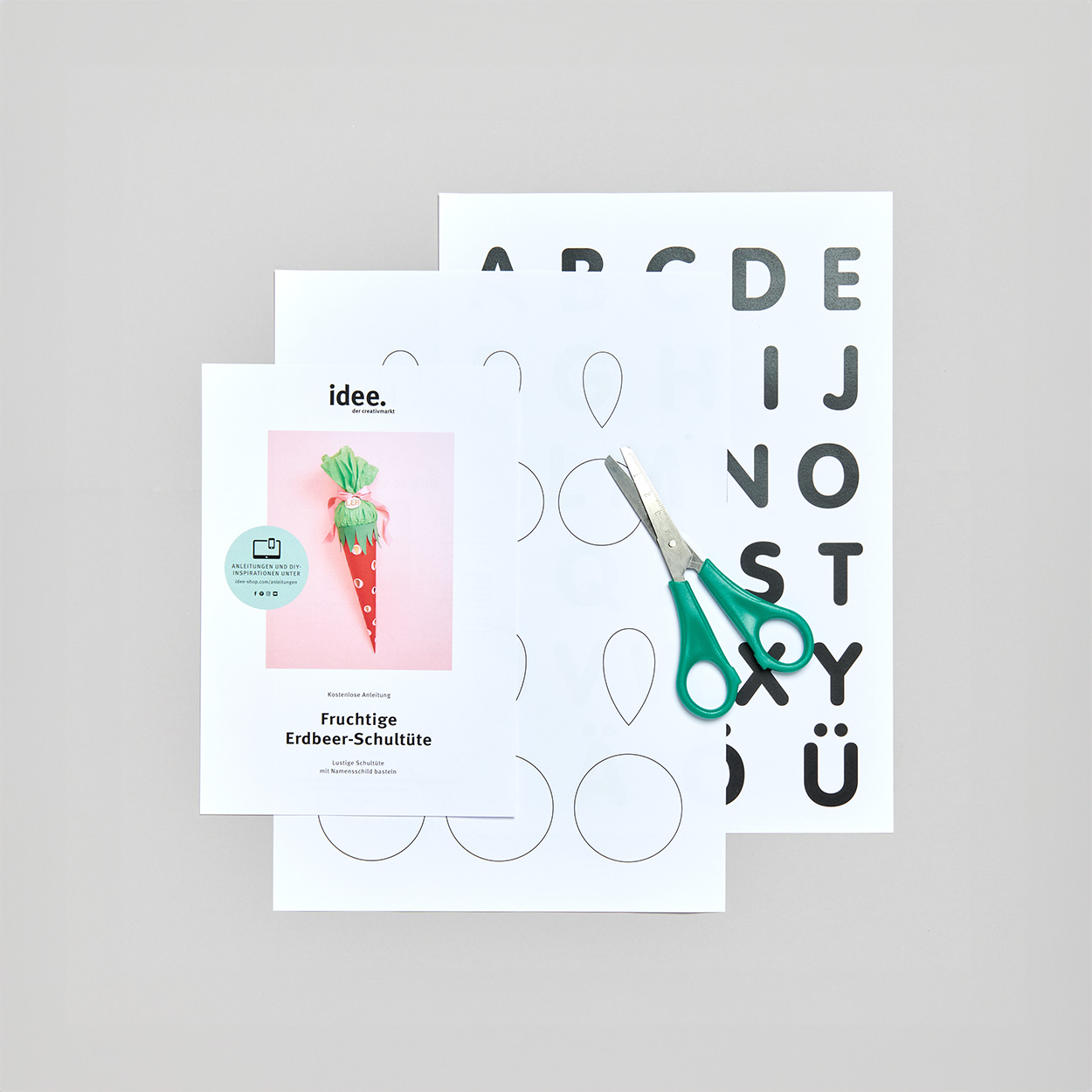 Anleitung zu einer Erdbeer-Schultüte mit dazugehöriger Vorlage mit Kreisen und Buchstaben, sowie eine Schere. Flatlay von Produkten.