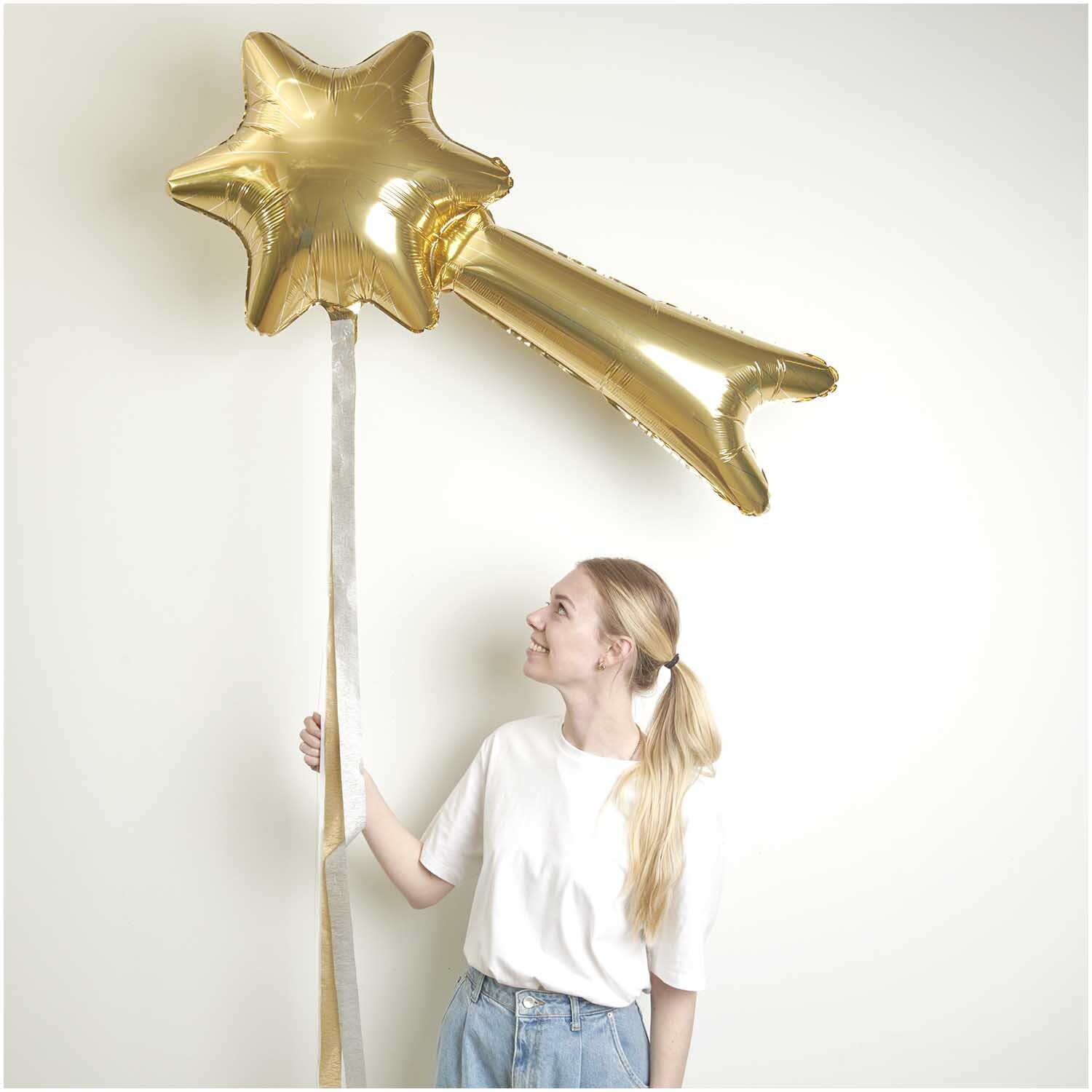 Folienballon Sternschnuppe in Gold von Rico Design, gehalten von einer Person vor weißem Hintergrund.